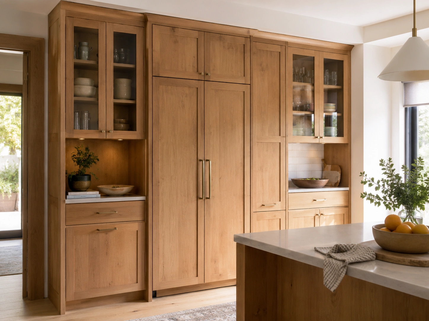 Tall alder pantry wall with panel-front fridge, glass cabinets, brass hardware, and white kitchen island.