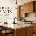 Warm alder kitchen cabinets with marble island, black hardware, pendant lights, and modern cream backsplash.