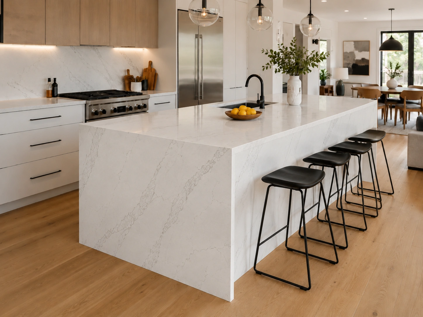 Waterfall edge quartz island in a modern open kitchen with black stools and wood cabinets.