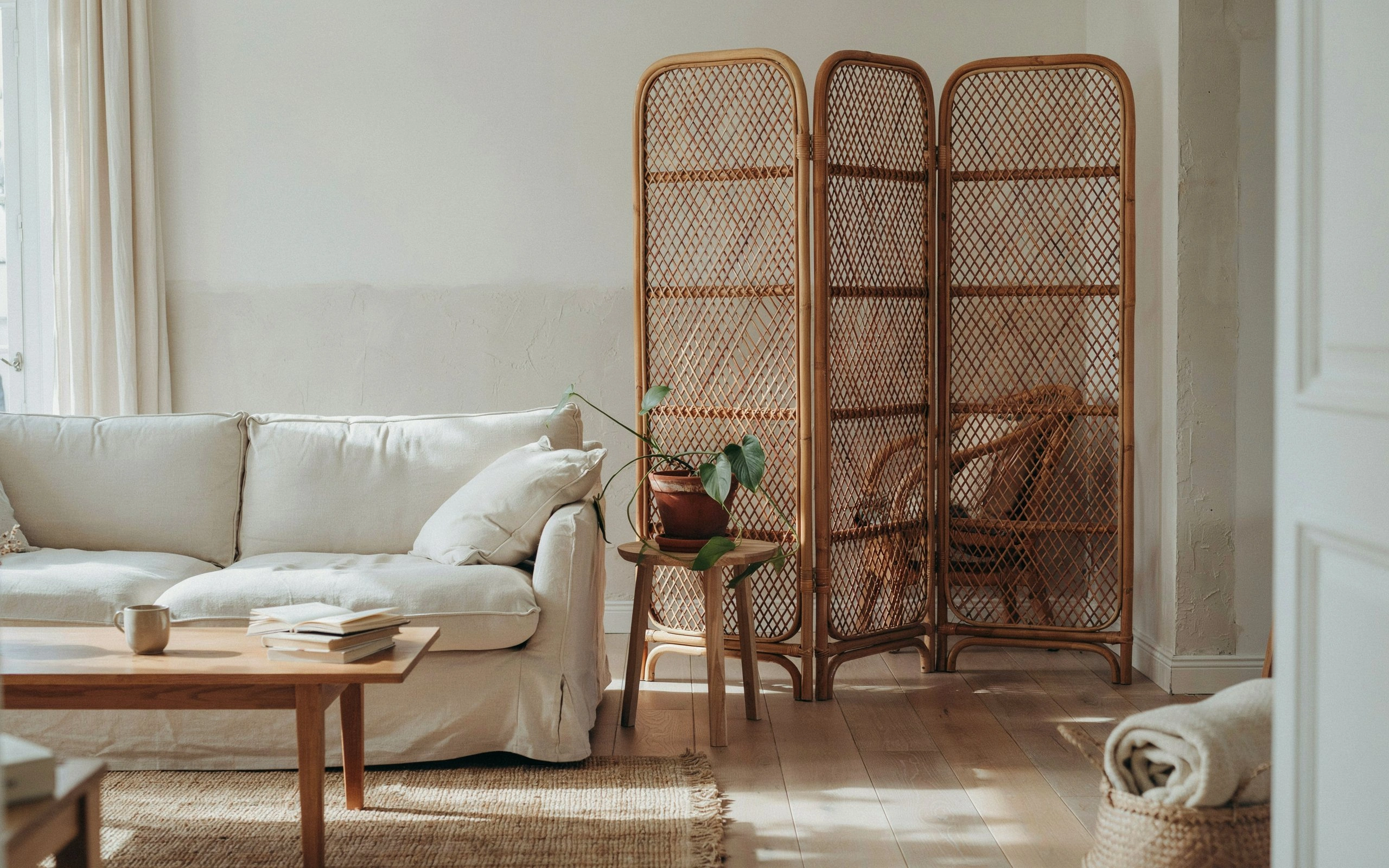 Woven rattan screen panel dividing a warm coastal boho living room with neutral sofa and wood accents.