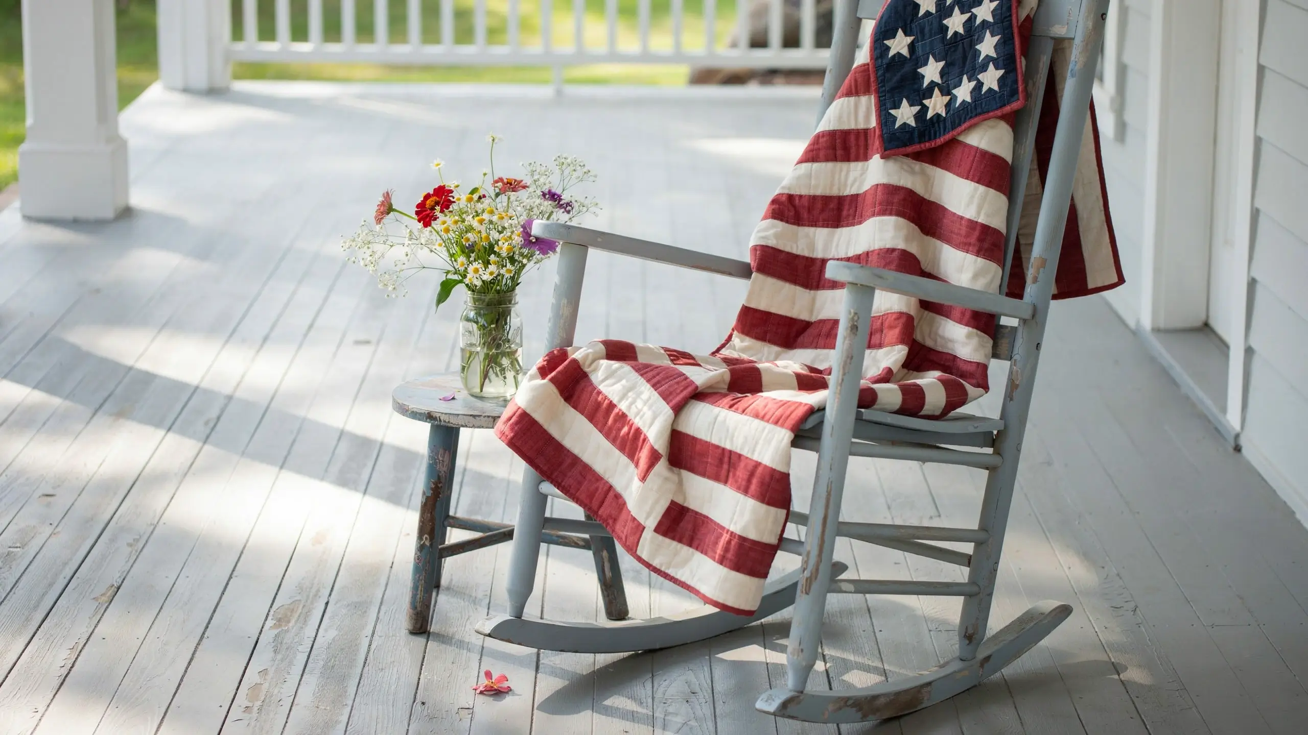 American flag lap quilt draped over a distressed wooden rocking chair, beside a wildflower mason jar on a sunny porch.