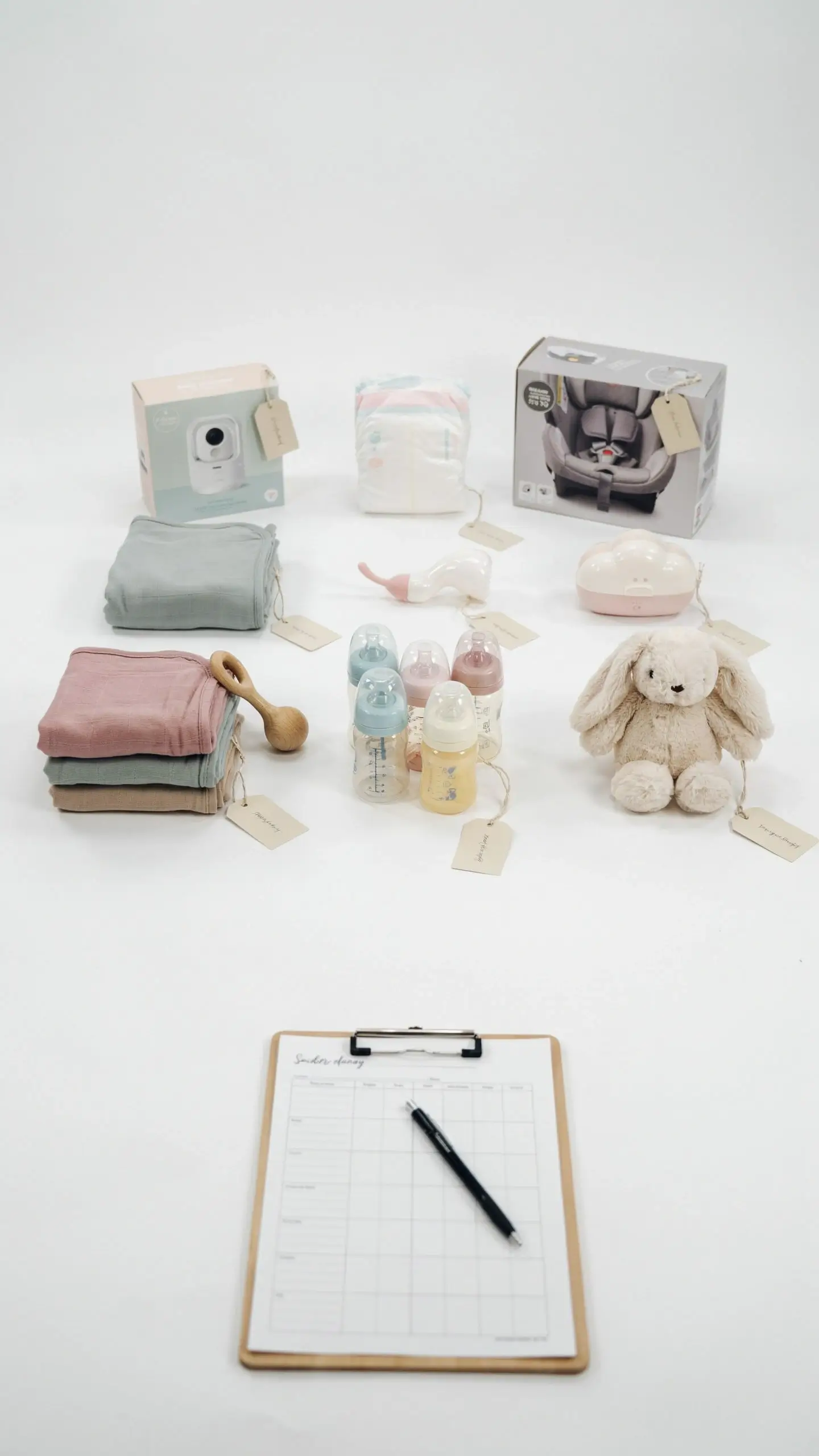 Baby Price Is Right shower game setup featuring a checklist clipboard, pastel baby bottles, swaddle blankets, and a plush bunny arranged on a white background. 