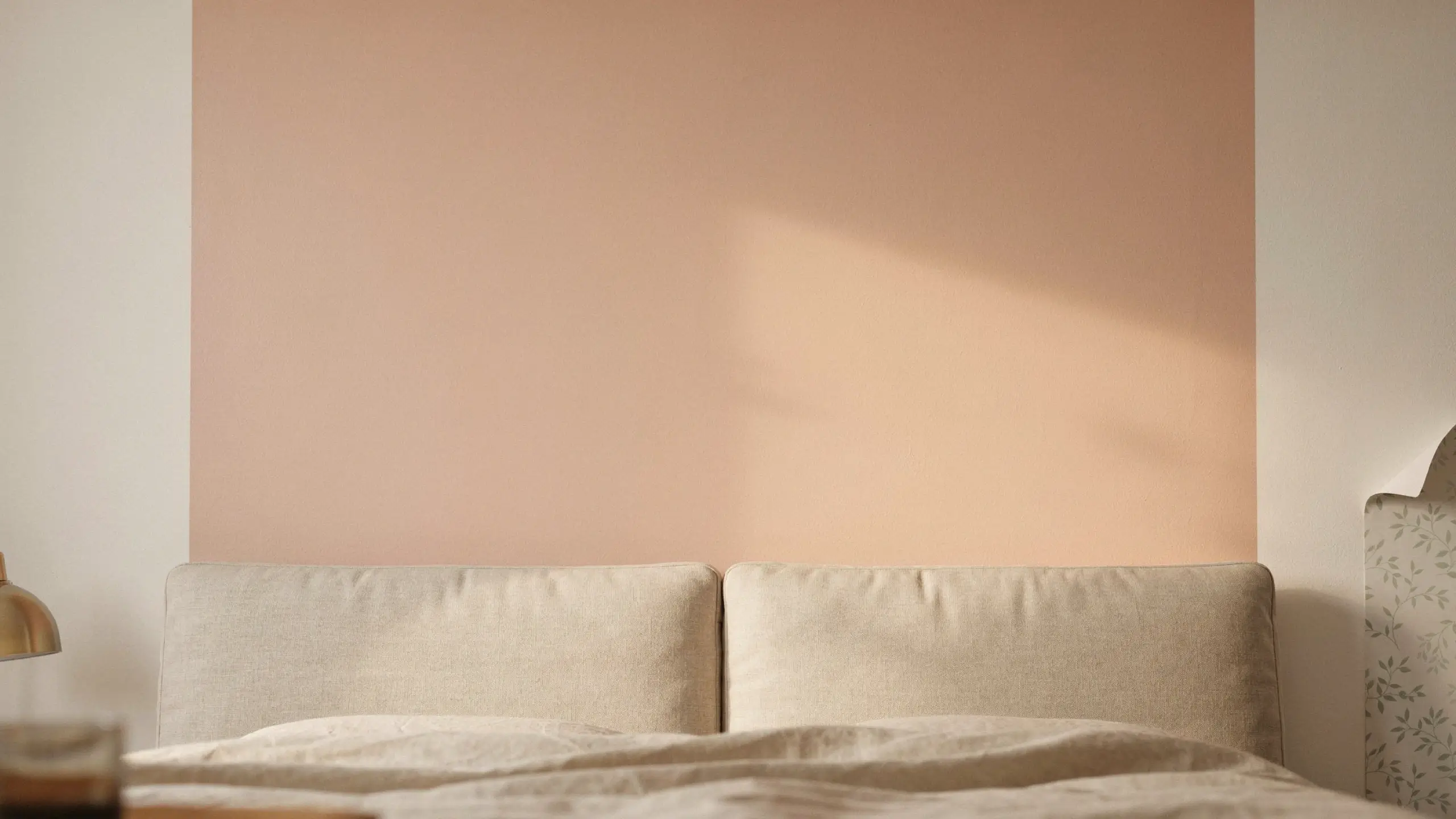 Minimalist bedroom with a low-commitment blush peach painted block accent wall, beige linen headboards, and a brass lamp. 