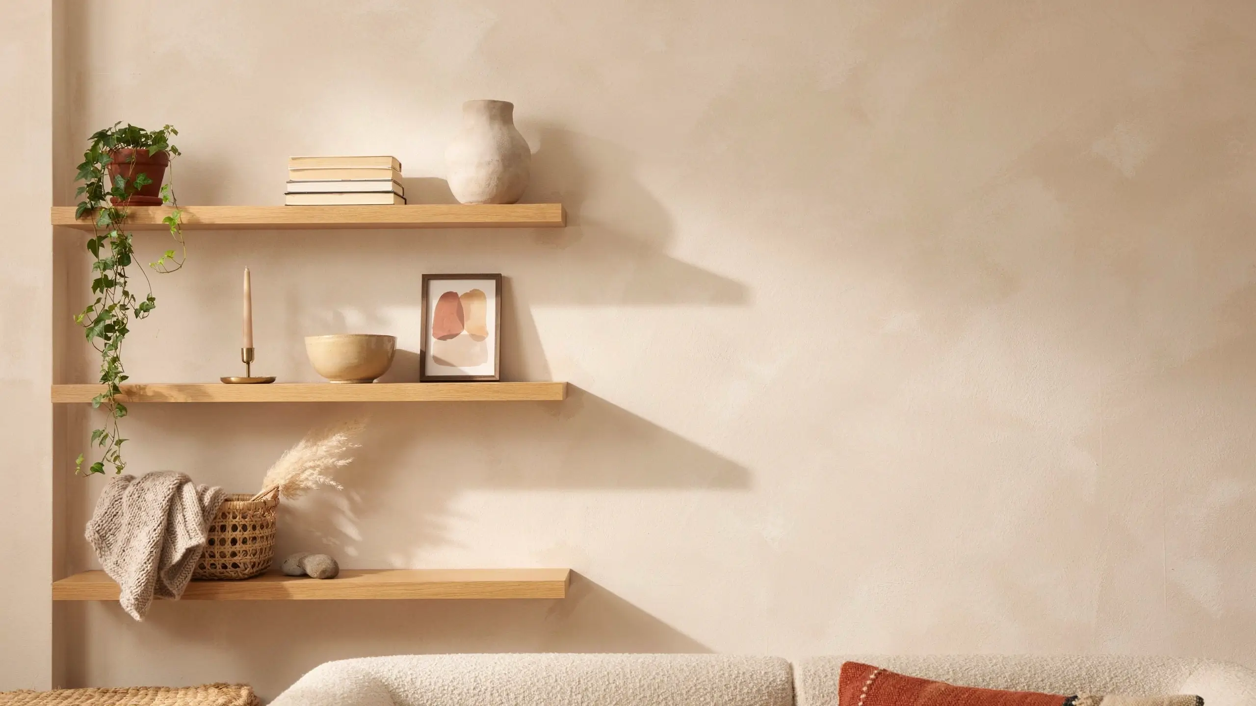 Sunlit boho living room with three wood shelves styled with books, pottery, plants, framed art, and woven decor.