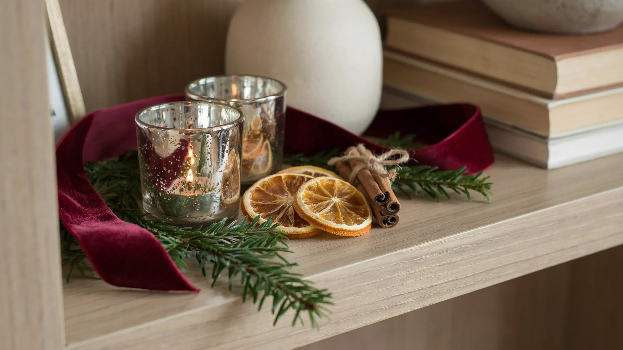 Christmas shelf decor with burgundy ribbon, mercury glass candleholders, dried citrus, cinnamon, and evergreen.