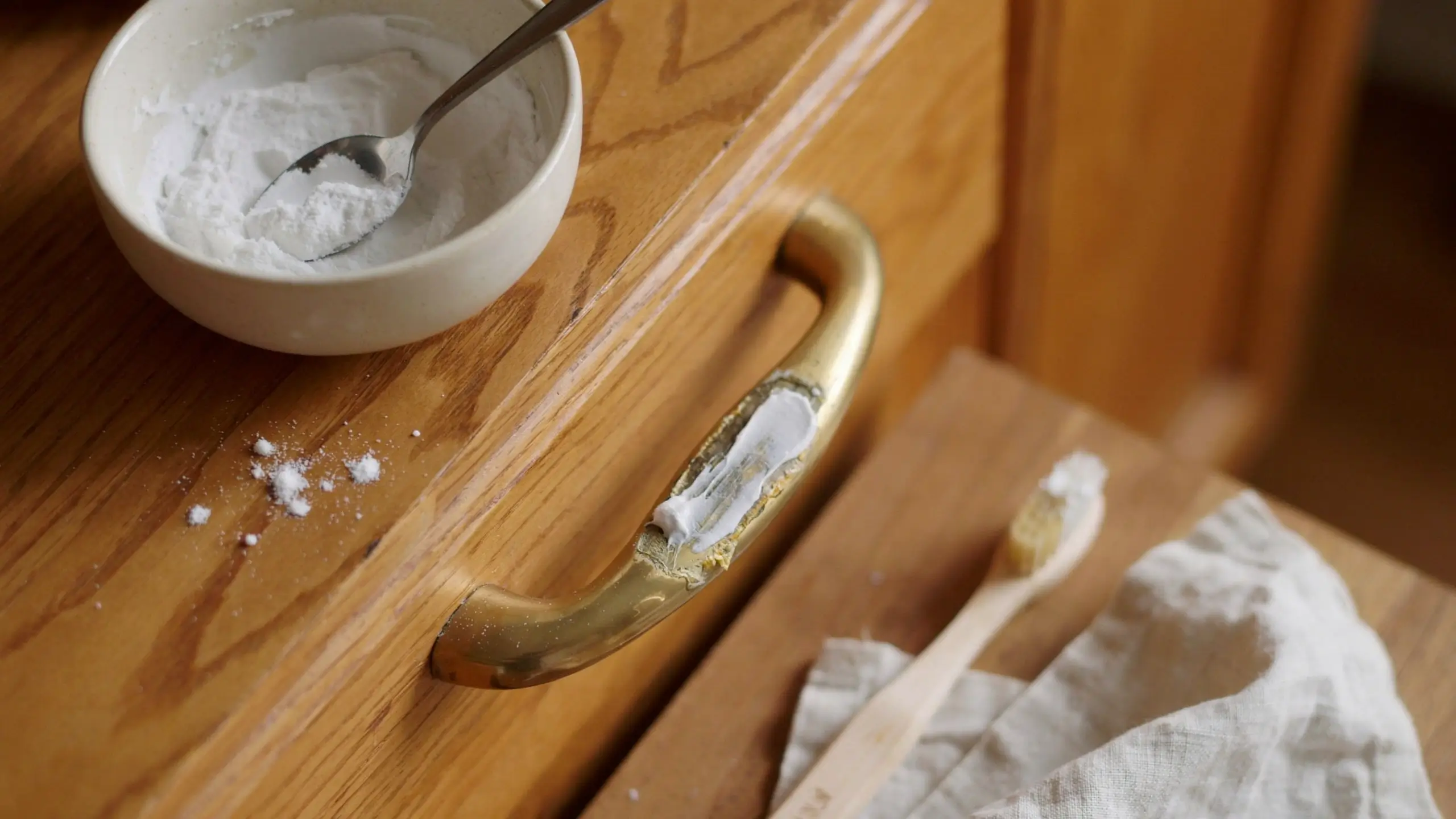 Applying a homemade baking soda paste to remove caked-on grime from a tarnished brass drawer handle on a wooden cabinet