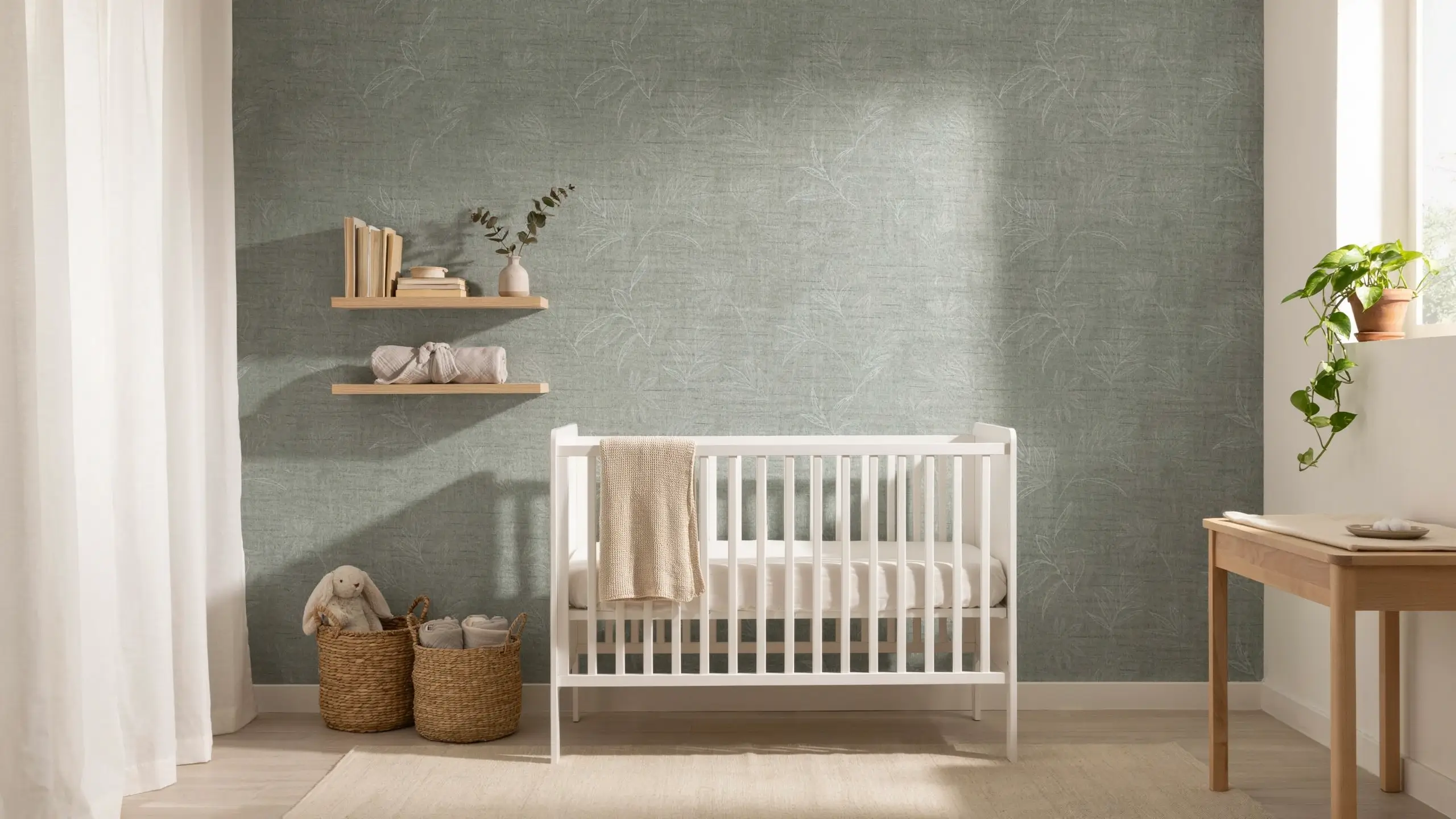 Sage green nursery with clustered botanical wall decals, white crib, floating shelves, woven baskets, and minimalist decor.