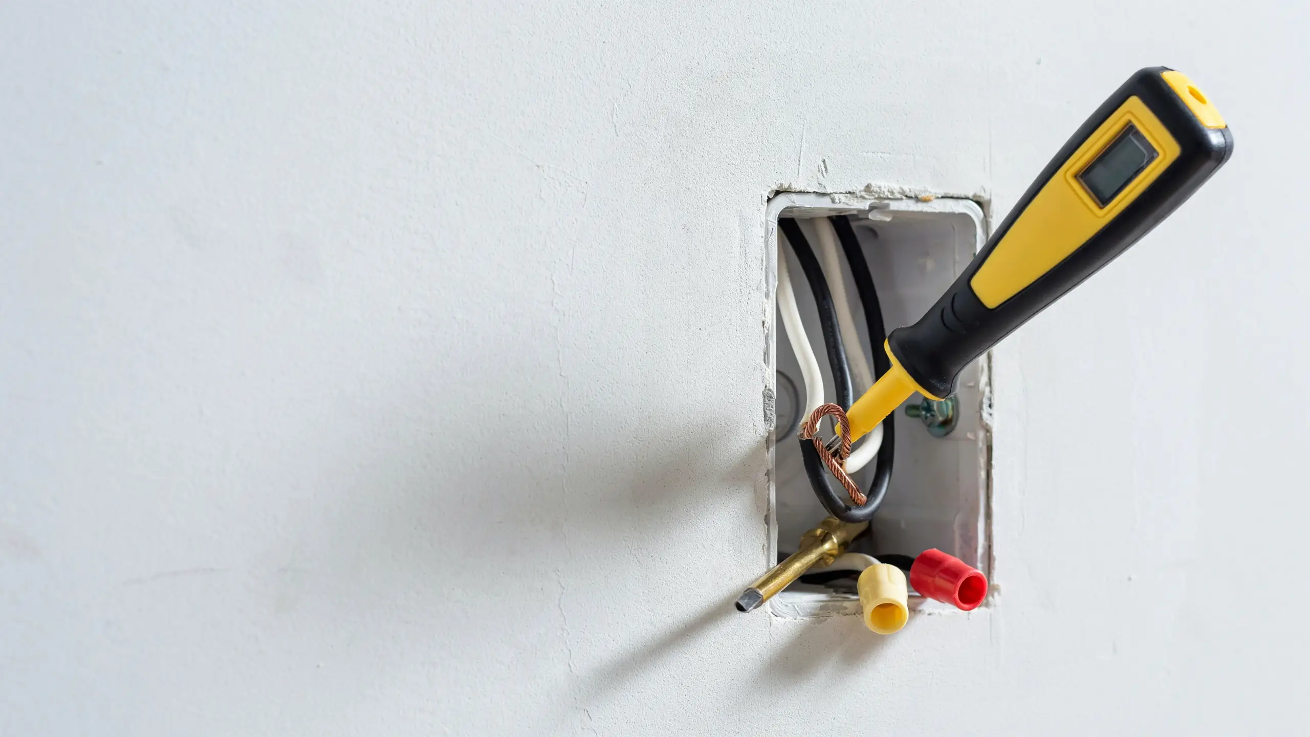 A non-contact voltage tester being used on exposed electrical wires inside a white wall outlet box during a DIY home repair to confirm the power supply is turned off.