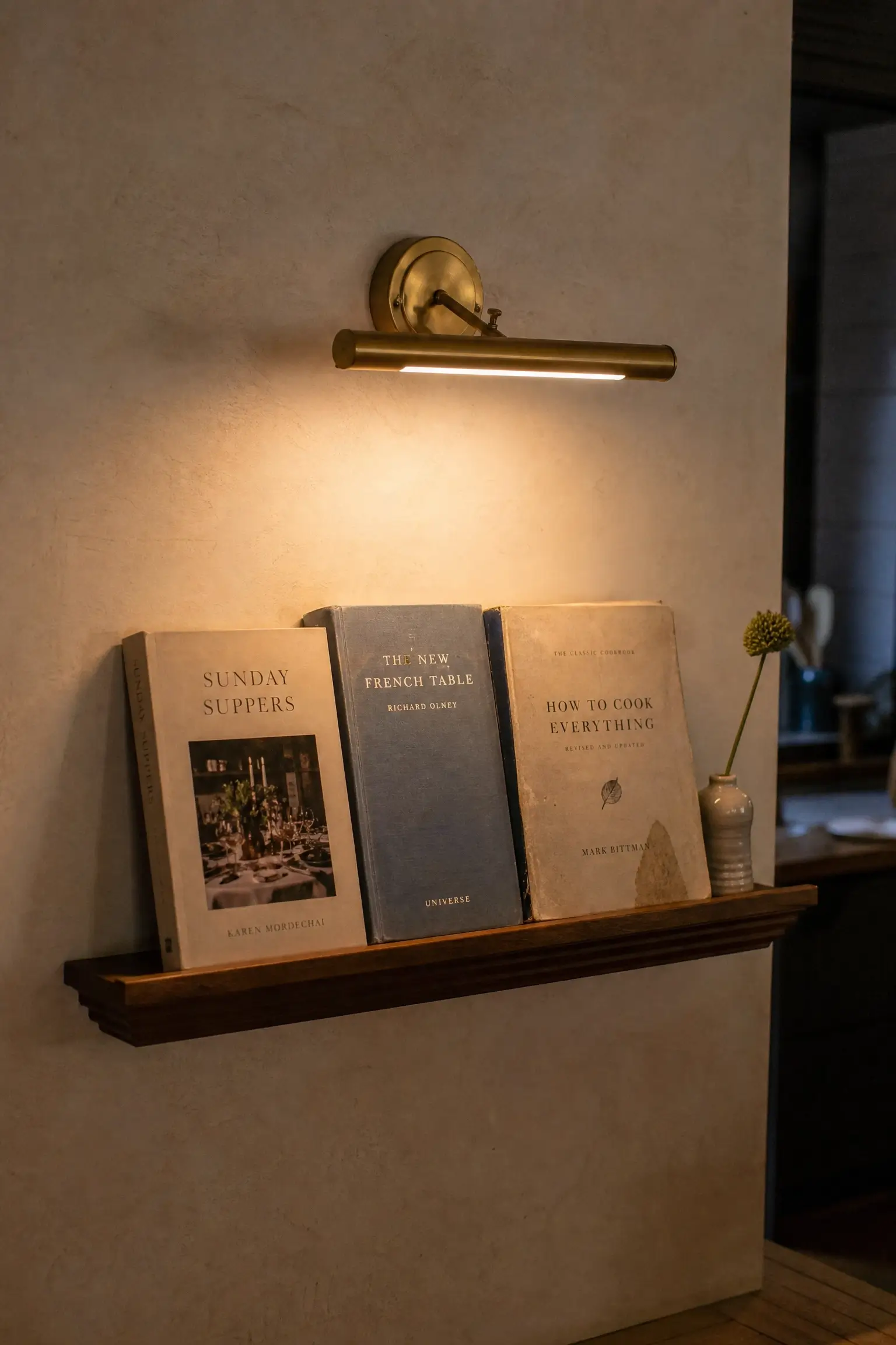A stacked display of cookbooks on an open shelf featuring Sunday Suppers by Richard Olney and How to Cook Everything by Mark Bittman, showcasing classic kitchen library decor. 