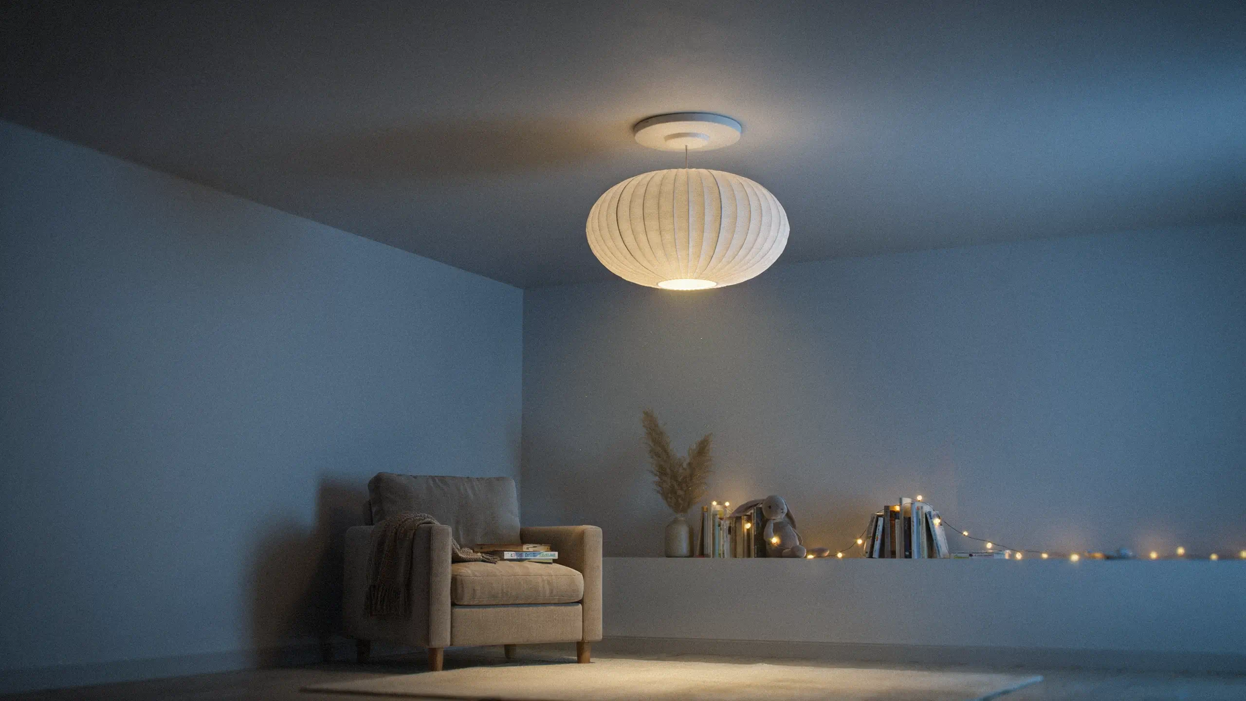 Cozy modern interior with a beige armchair, books, and a ribbed white paper pendant light illuminating a minimalist shelf with warm fairy lights and pampas grass. 