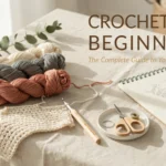 Crochet for Beginners: The Complete Guide to Learning Your First Stitches A flat lay of crochet supplies for a beginner's guide, featuring cream, grey, and terracotta yarn skeins, a wooden crochet hook, a finished practice swatch, and a notebook with stitch diagrams on a linen tablecloth.