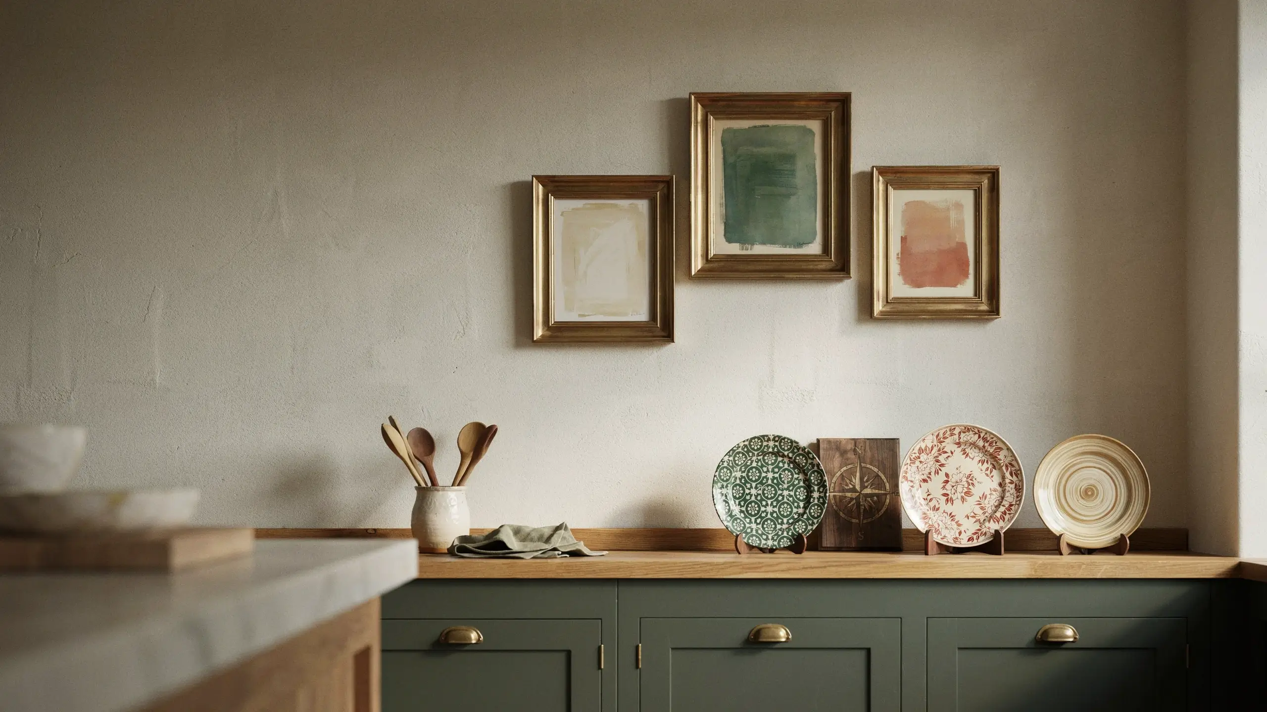 Curated personal collection of framed art and decorative plates above green kitchen cabinets