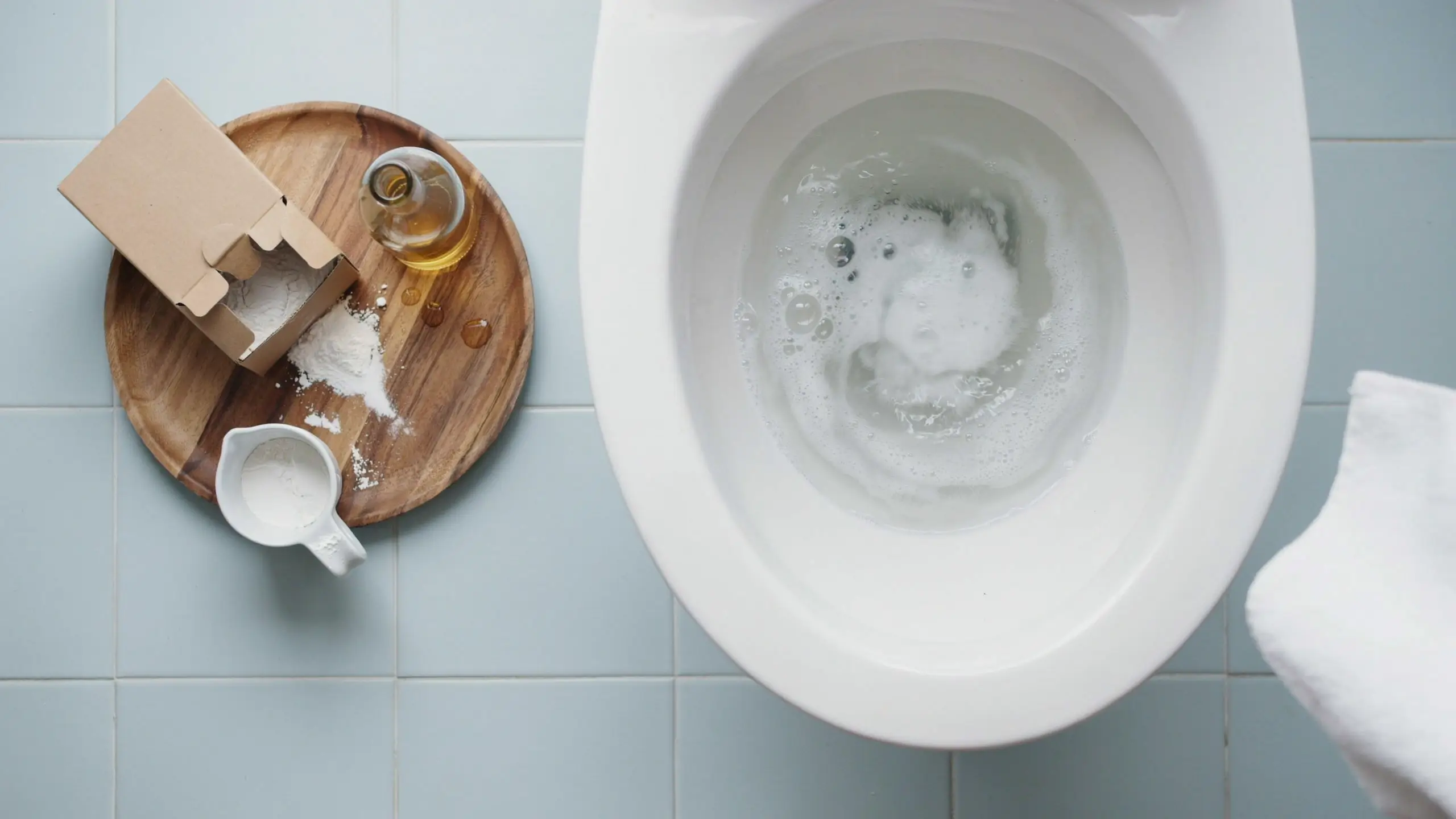 Top view of baking soda and white vinegar creating a reactive foam inside a white toilet bowl for a natural, eco-friendly cleaning method.
