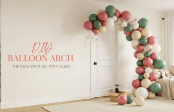 A DIY balloon arch in sage green, dusty rose, and cream colors installed next to a white door in a modern living room, with a balloon pump and supplies on the floor, illustrating an easy step-by-step party decoration tutorial