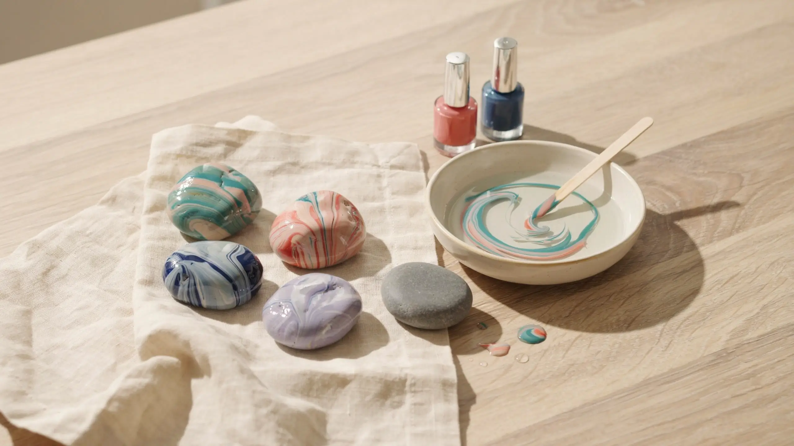 Colorful marbled paperweight rocks beside a bowl of swirled nail polish and water.