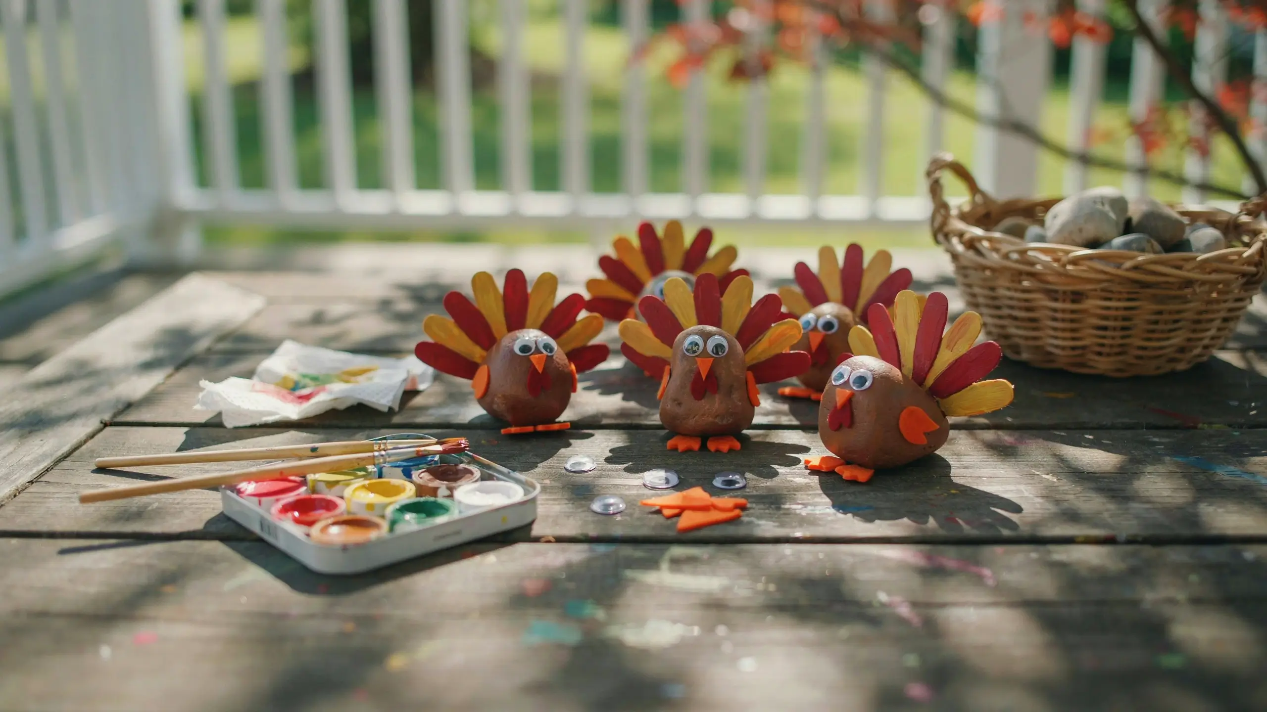 Hand-painted rock turkeys with googly eyes on a wooden deck with paint supplies for a fall craft.