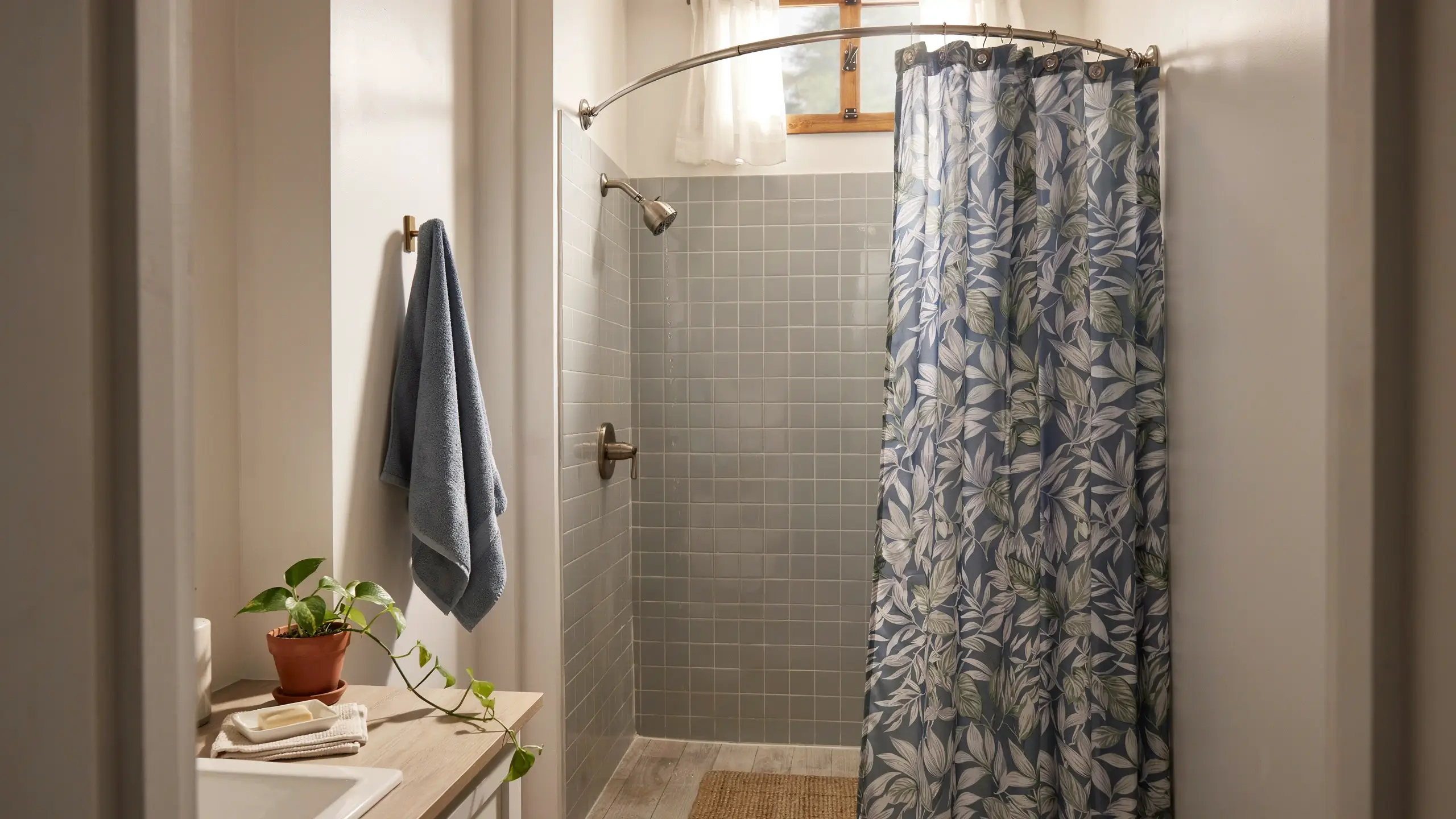 A blue botanical pattern fabric shower curtain hung on a curved rod in a small camper bathroom with gray subway tiles and a wooden counter. 