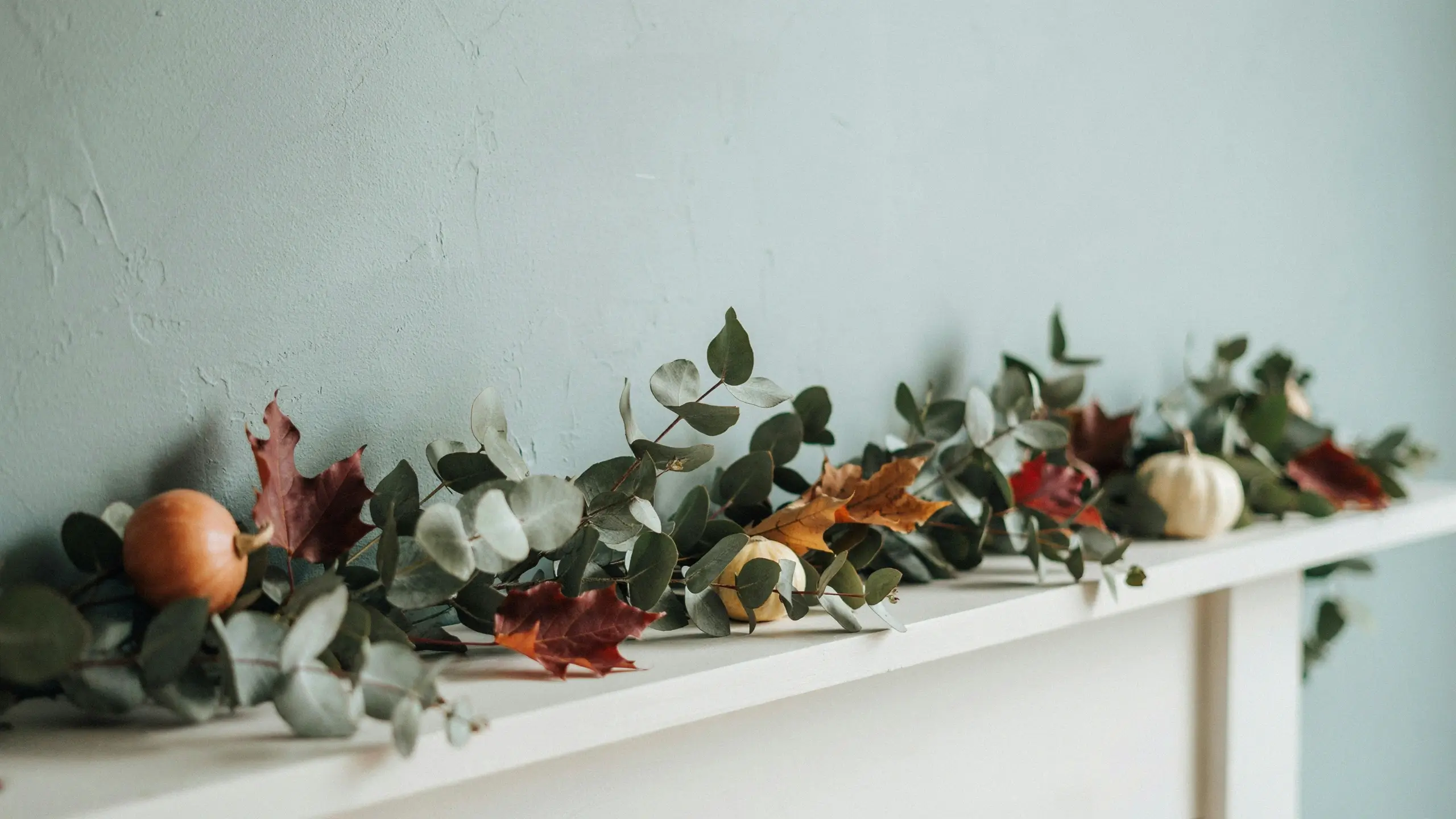 Modern fall mantle decor with eucalyptus garland, autumn maple leaves, and small orange, yellow, and white pumpkins on a white shelf." Finally, for context-rich ranking, embed an