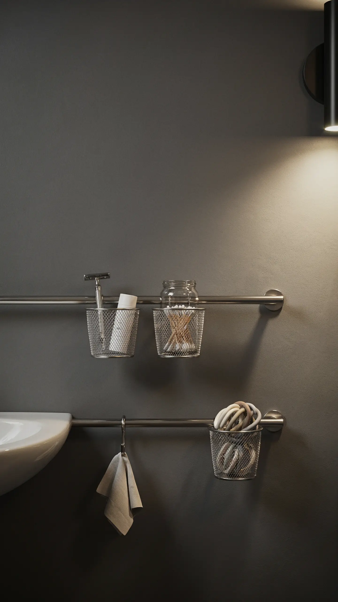 IKEA FINTORP stainless steel rail with mesh baskets storing a razor, cotton swabs, and towel on a dark gray minimalist bathroom wall. 