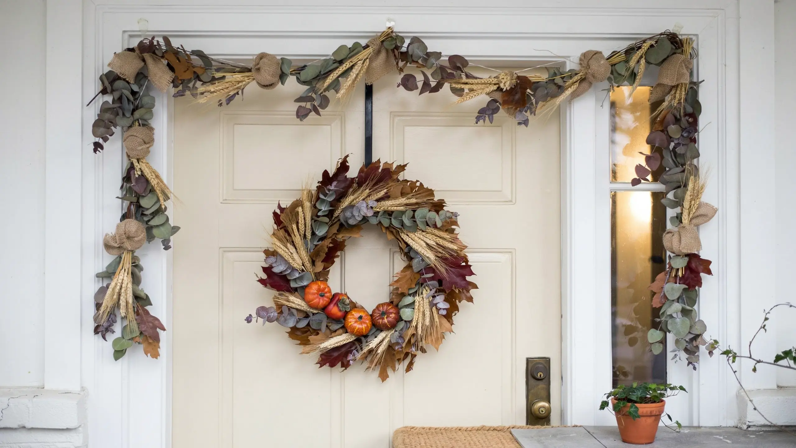 Alt Text: Foraged fall wreath and eucalyptus garland decorating a white front door with mini pumpkins and dried wheat