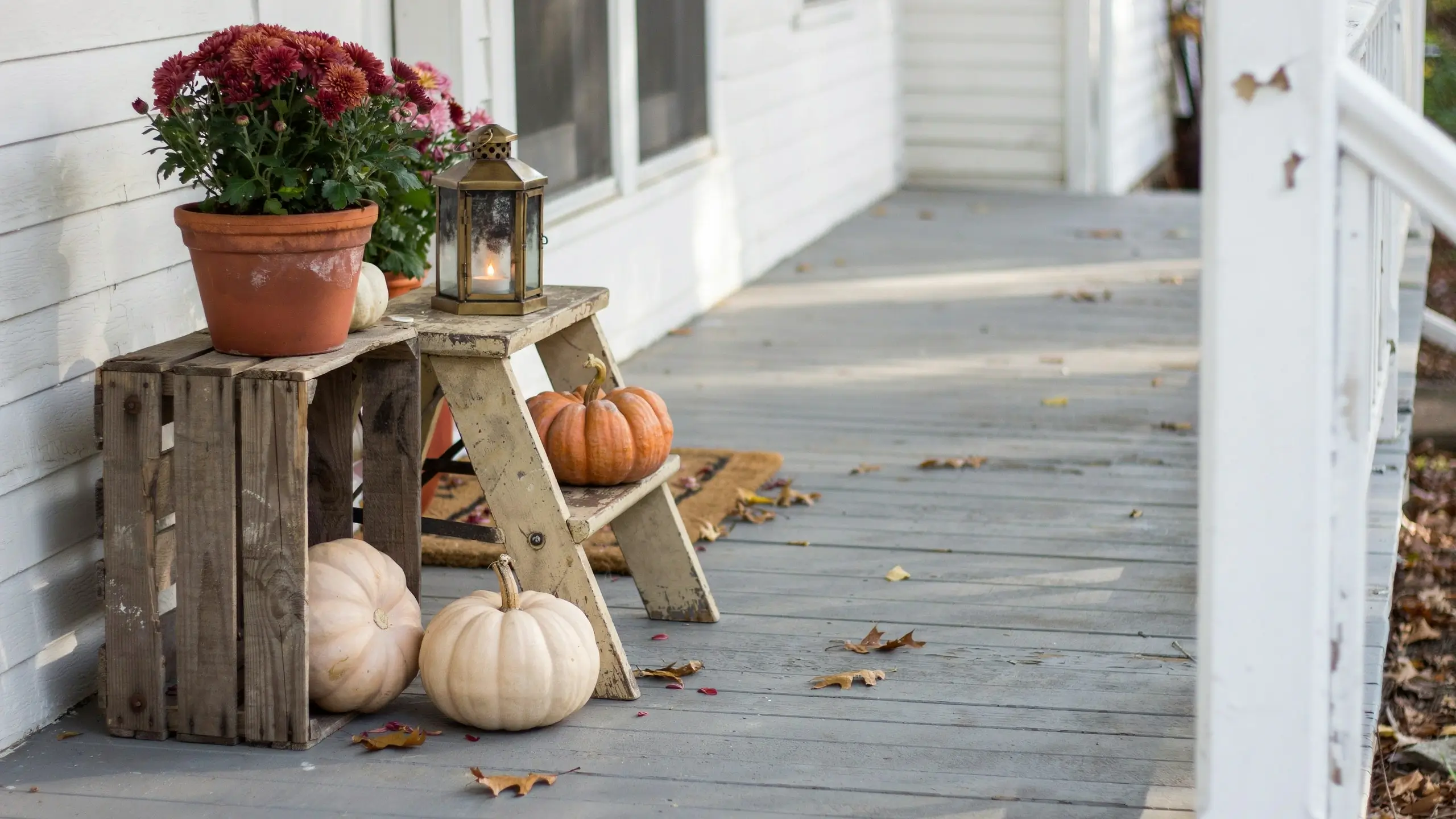 Wooden crate and old step stool used as risers for pumpkins, mums, and a lantern on a fall front porch.