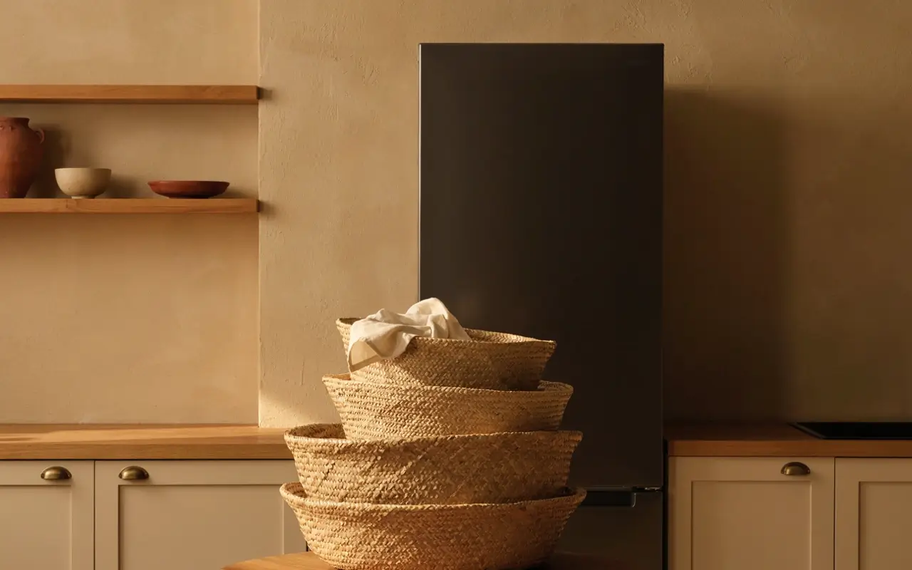 Graduated stack of woven baskets arranged in a warm neutral kitchen beside a black refrigerator.