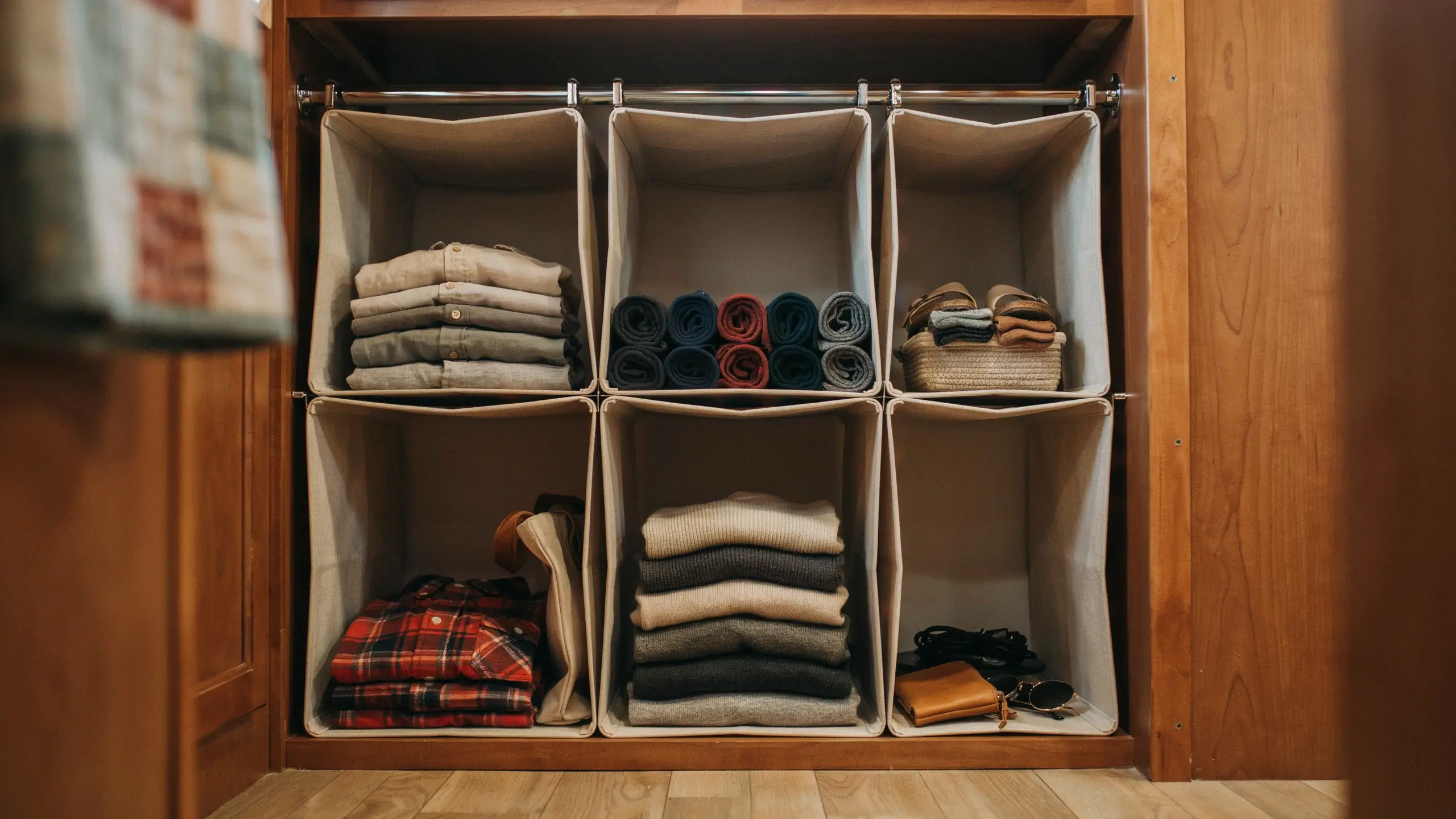 Beige fabric hanging closet organizer holding folded shirts, rolled socks, and accessories inside a wooden wardrobe for vertical storage.