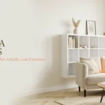 Bright small living room featuring a white floating IKEA shelving unit hack styled with minimal decor, next to a textured beige armchair and round wooden coffee table.