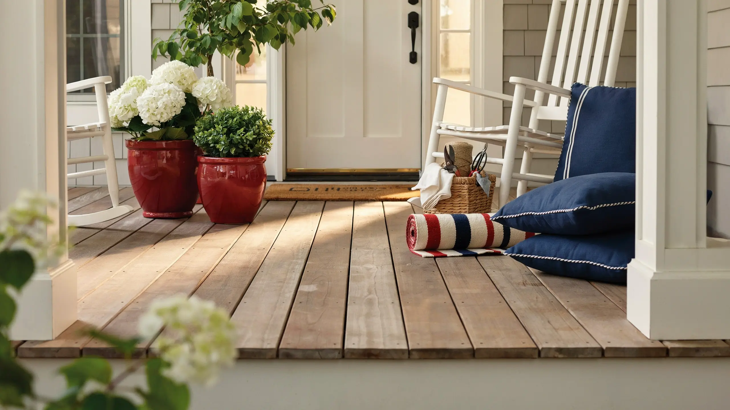 Patriotic front porch with red planters, white hydrangeas, navy cushions, and a striped outdoor rug.