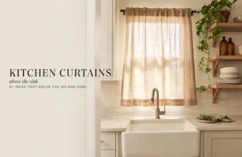 Beige linen kitchen curtains above a farmhouse sink with open shelves and trailing plant.