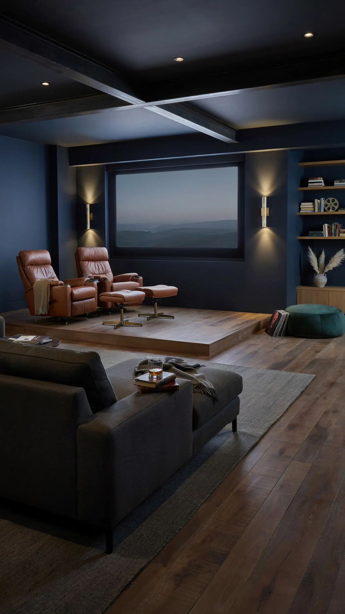 Layered seating arrangement in a home theater featuring tan leather recliners on a raised wooden platform and a dark grey sofa in the foreground. 