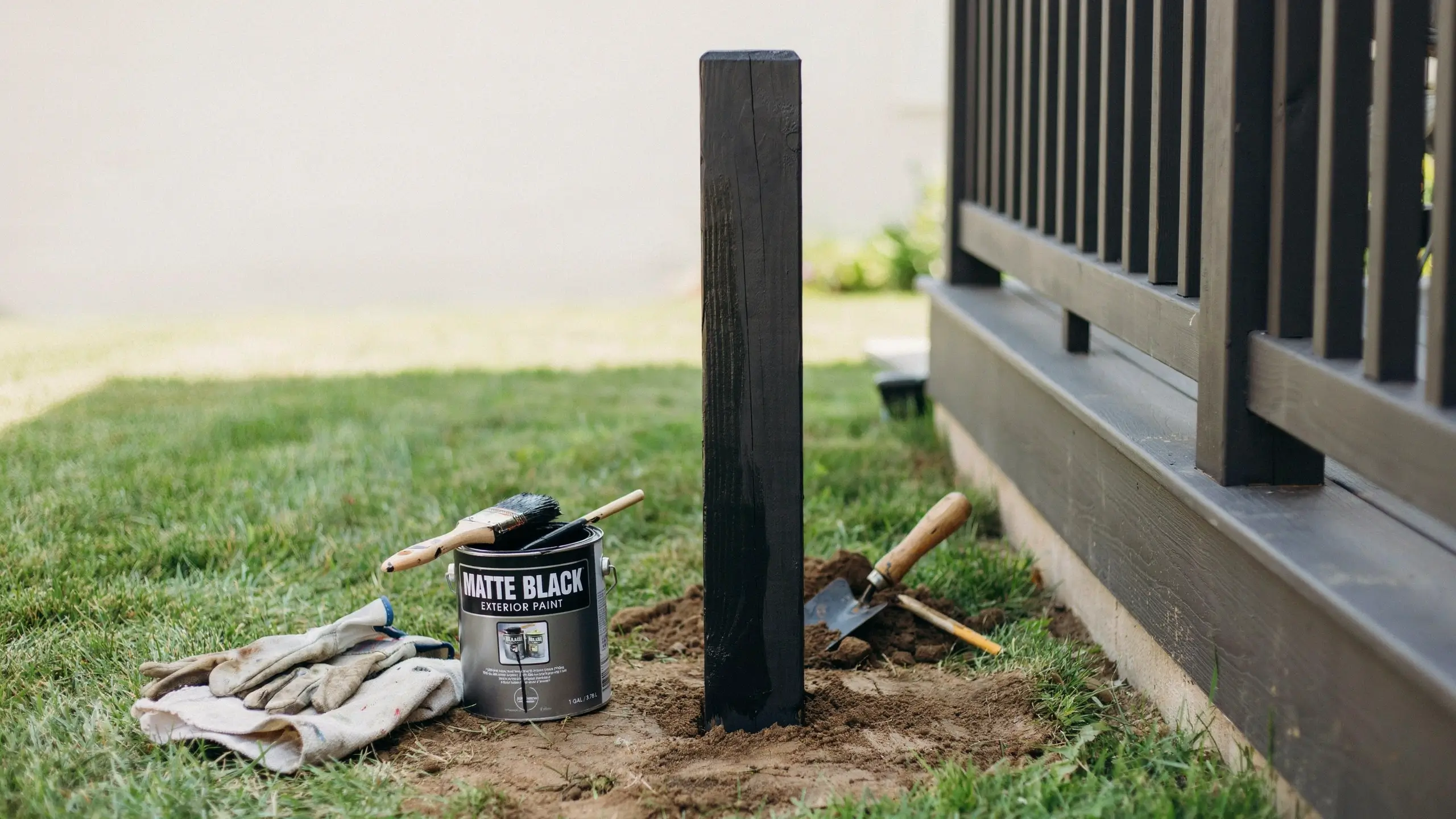 Matte black exterior paint applied to a wooden post before setting it into the ground for a durable, modern outdoor finish.
