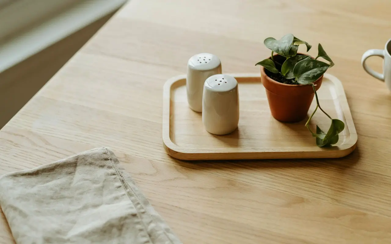 Mini wood tray with salt, pepper, and a small potted plant on a light wood dining table.