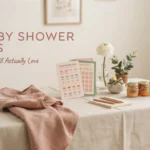 A minimalist baby shower game station featuring a 'Guess the Baby Food' tasting card and a 'Baby Bingo' sheet, paired with wooden pencils, a white notepad, three labeled baby food jars, and a soft pink draped napkin on a beige linen table.