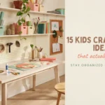 A bright, organized kids craft room featuring a white wooden table, a wall-mounted pegboard with scissors and tape, and floating shelves with pastel pink and green storage bins for paper and art supplies, with a corkboard displaying children's artwork.