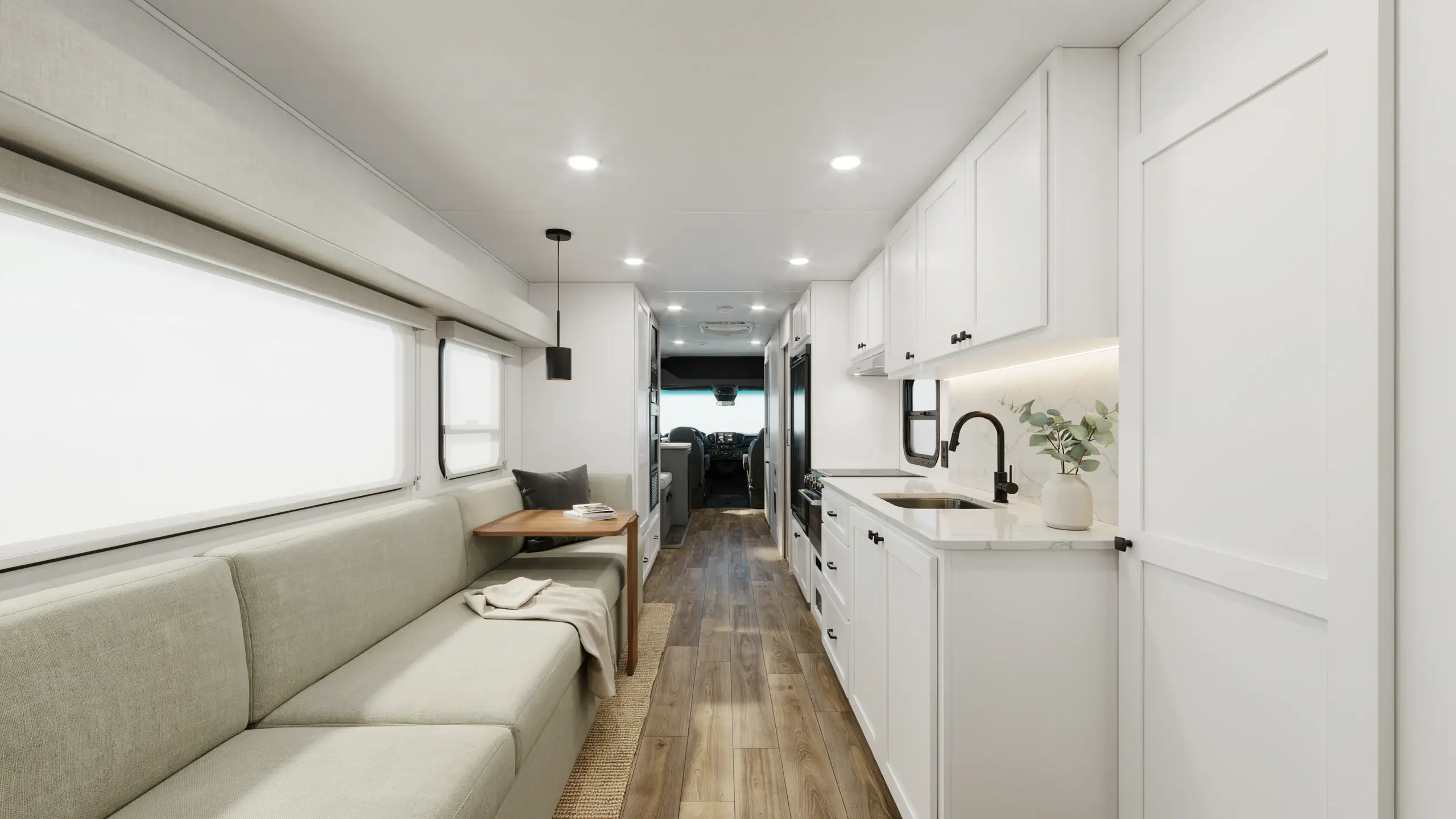 Bright modern minimalist RV interior featuring white shaker cabinets, beige sofa seating, wood floors, and a black faucet in a compact campervan kitchen. 