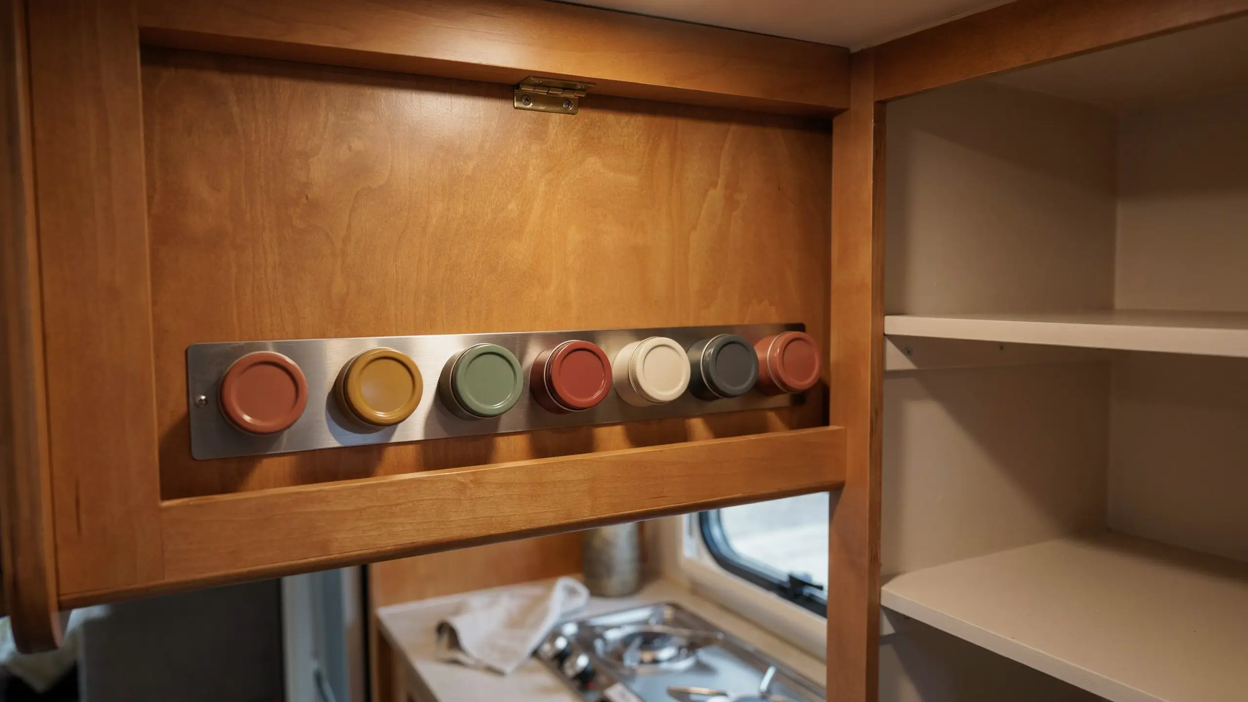 Magnetic spice strip mounted inside a kitchen cabinet door holding metal spice tins