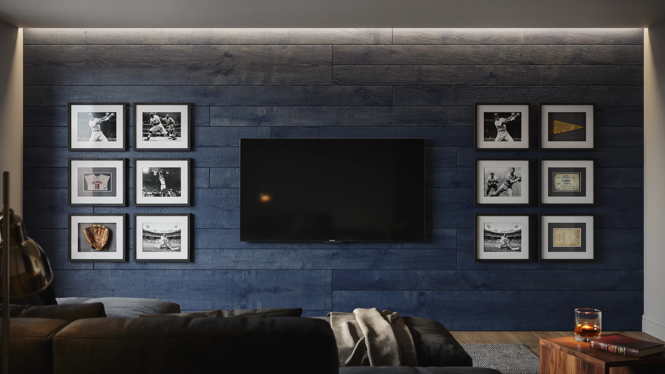 Dark navy blue horizontal wood paneling accent wall with a center flat-screen TV, surrounded by a symmetrical gallery of baseball memorabilia and photos in black frames, set above a grey sofa. 
