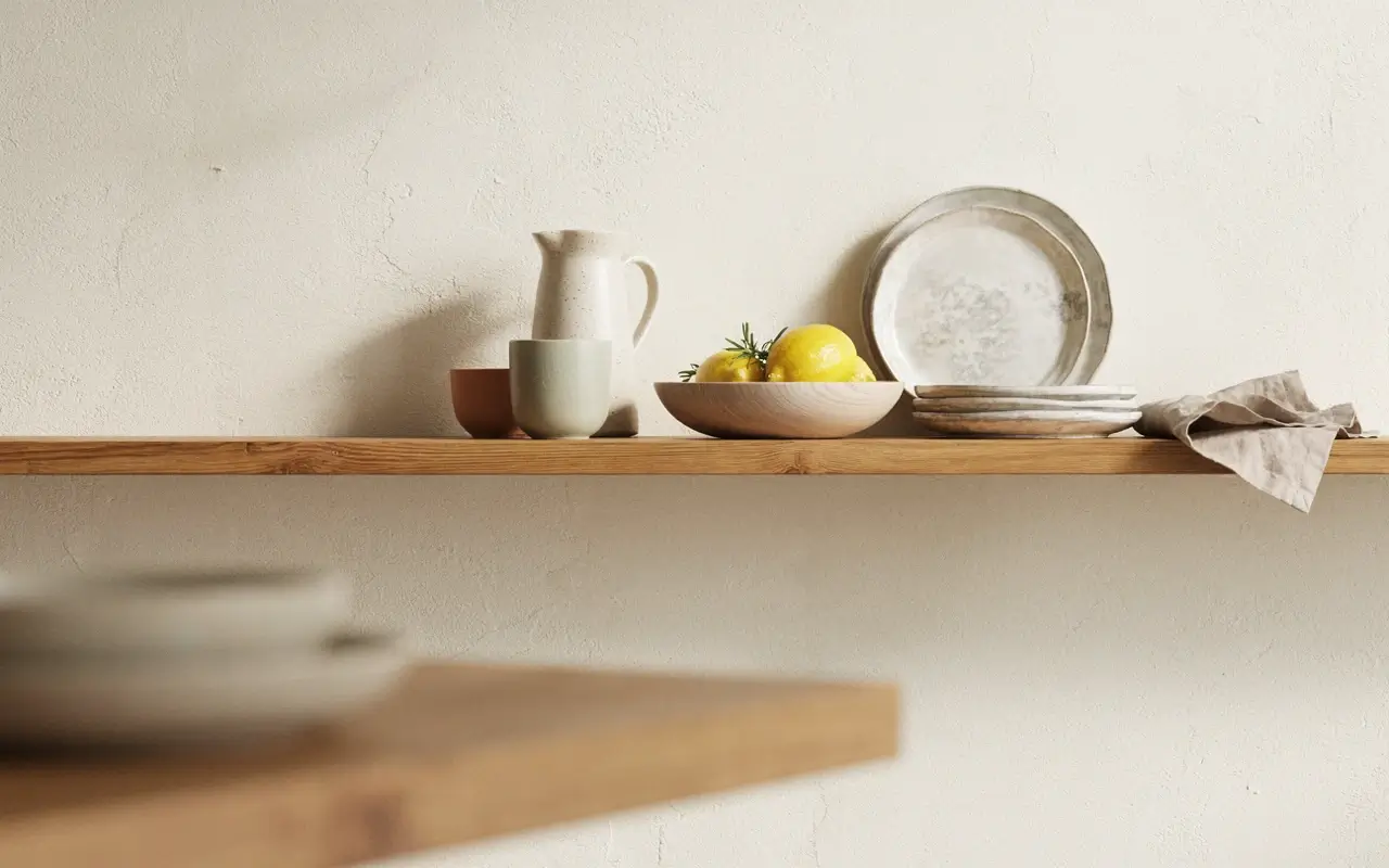 Open wooden kitchen shelf styled with clustered pottery, stacked plates, lemons, and wood bowls.