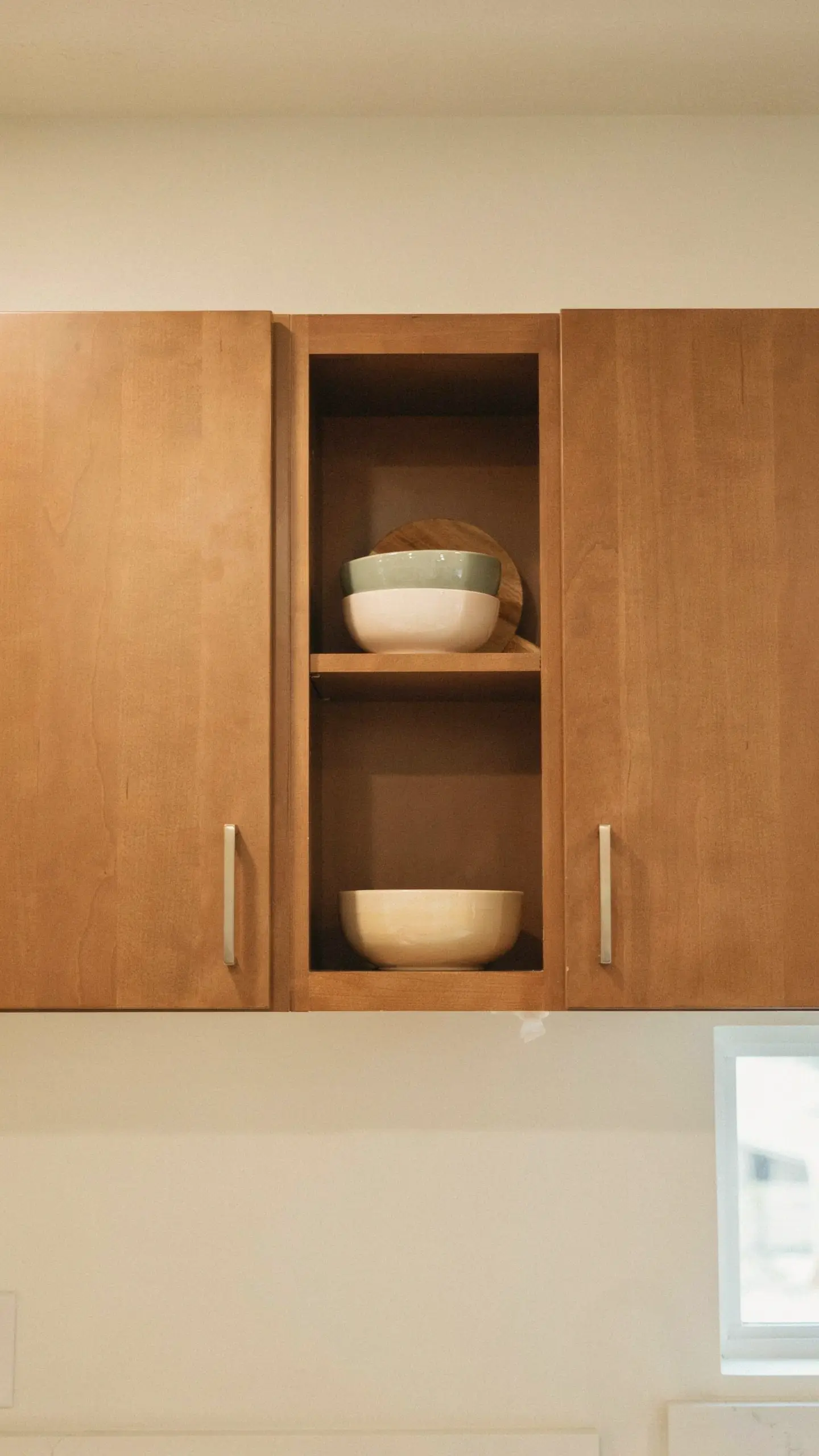 Wood upper kitchen cabinet with one door removed to create an open-shelf nook for bowls.