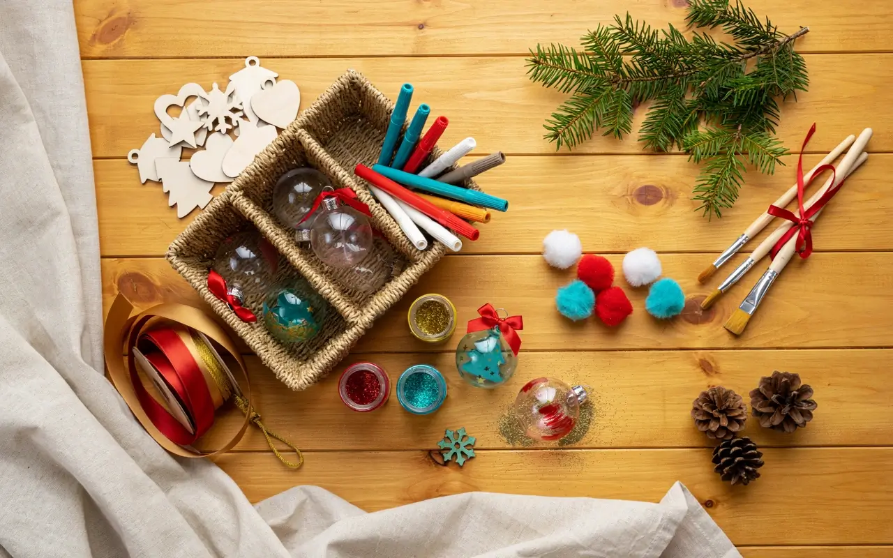 DIY Christmas ornament-making supplies with clear baubles, paint pens, glitter, ribbons, pom-poms, brushes and pinecones.
