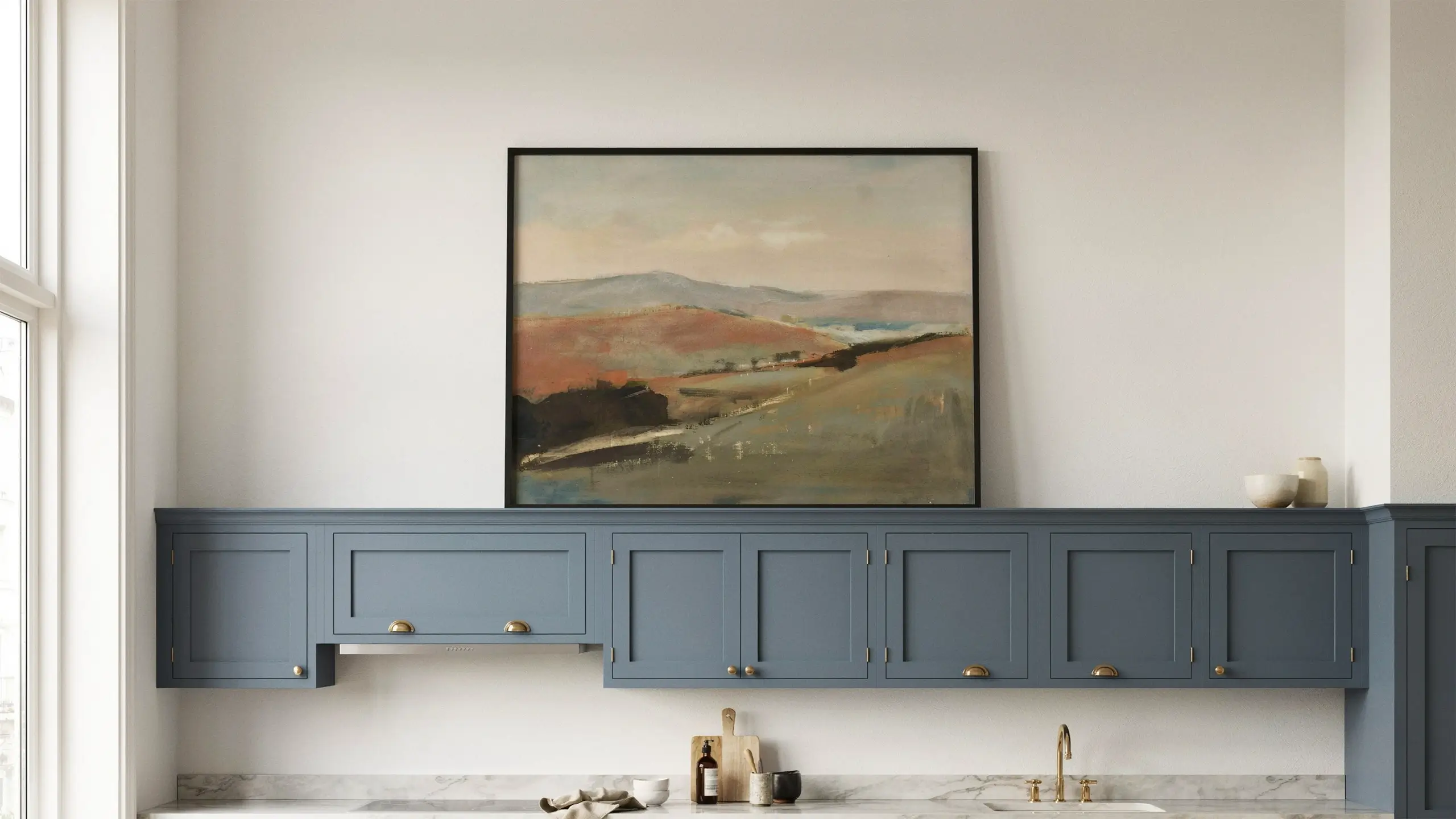 Oversized vintage landscape painting displayed above blue-gray kitchen cabinets.