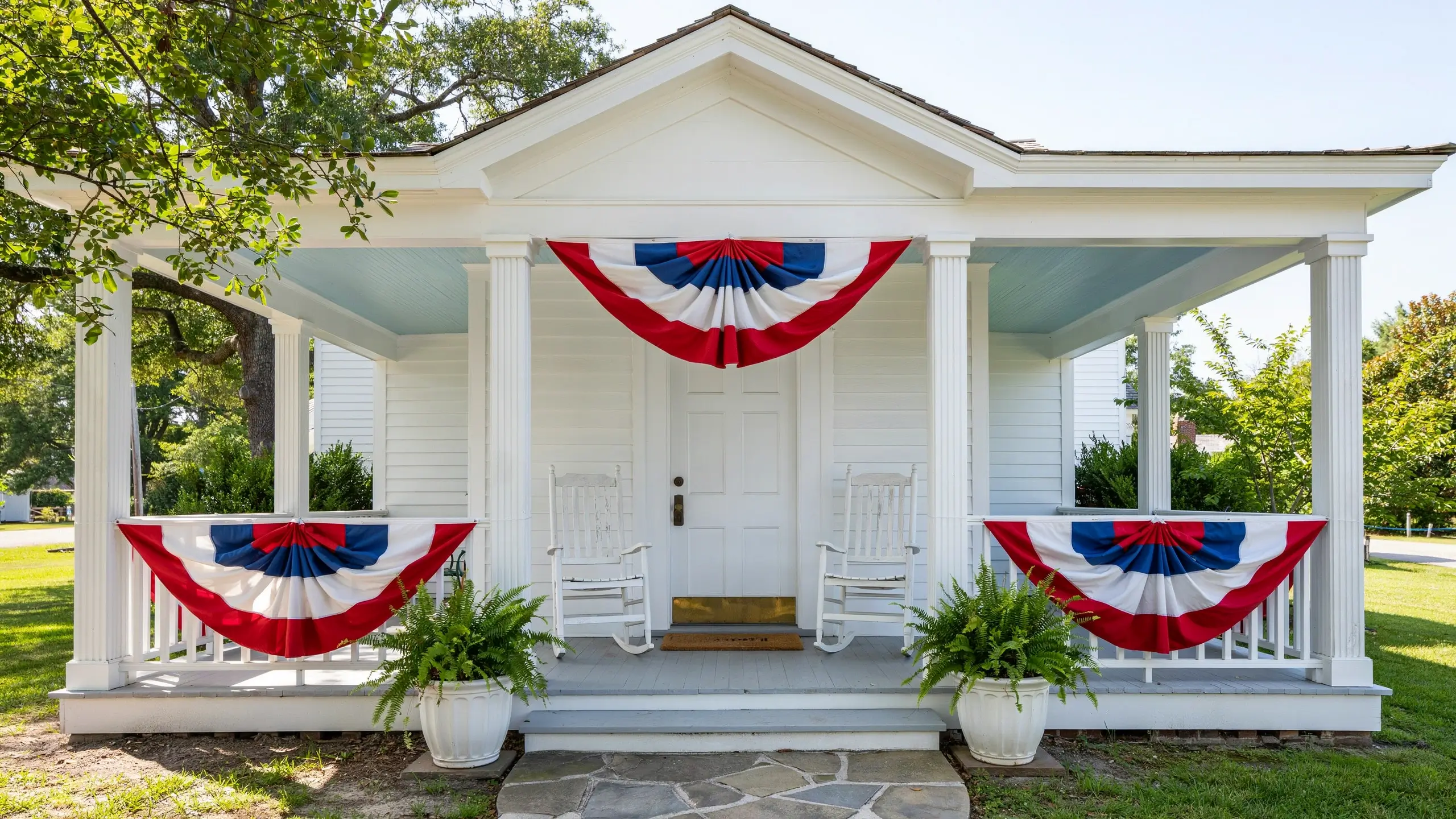 Red, white, and blue fan bunting hung above a front door on a patriotic Fourth of July porch.