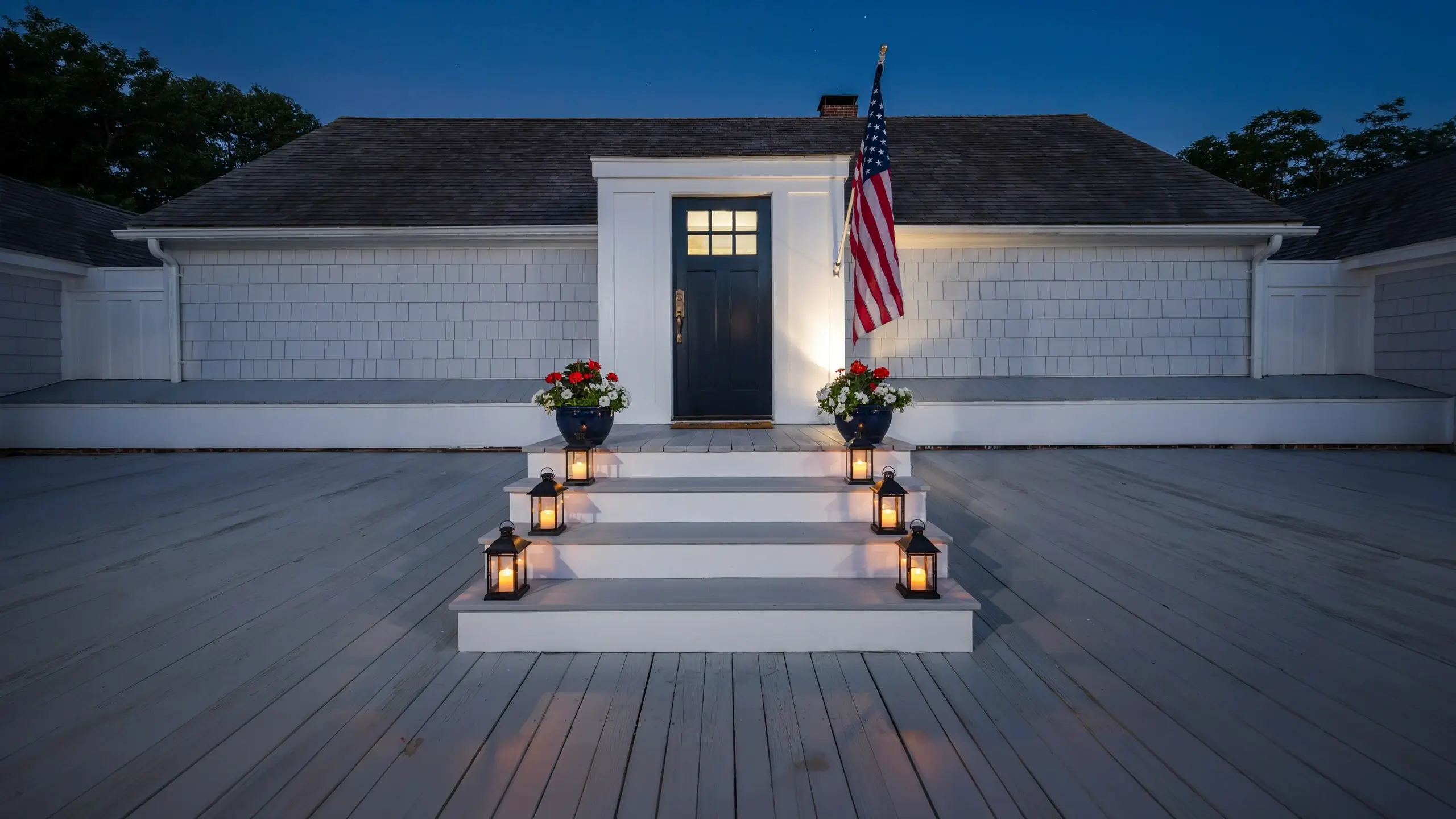 Patriotic front porch steps lined with glowing lanterns beside an illuminated American flag at dusk.
