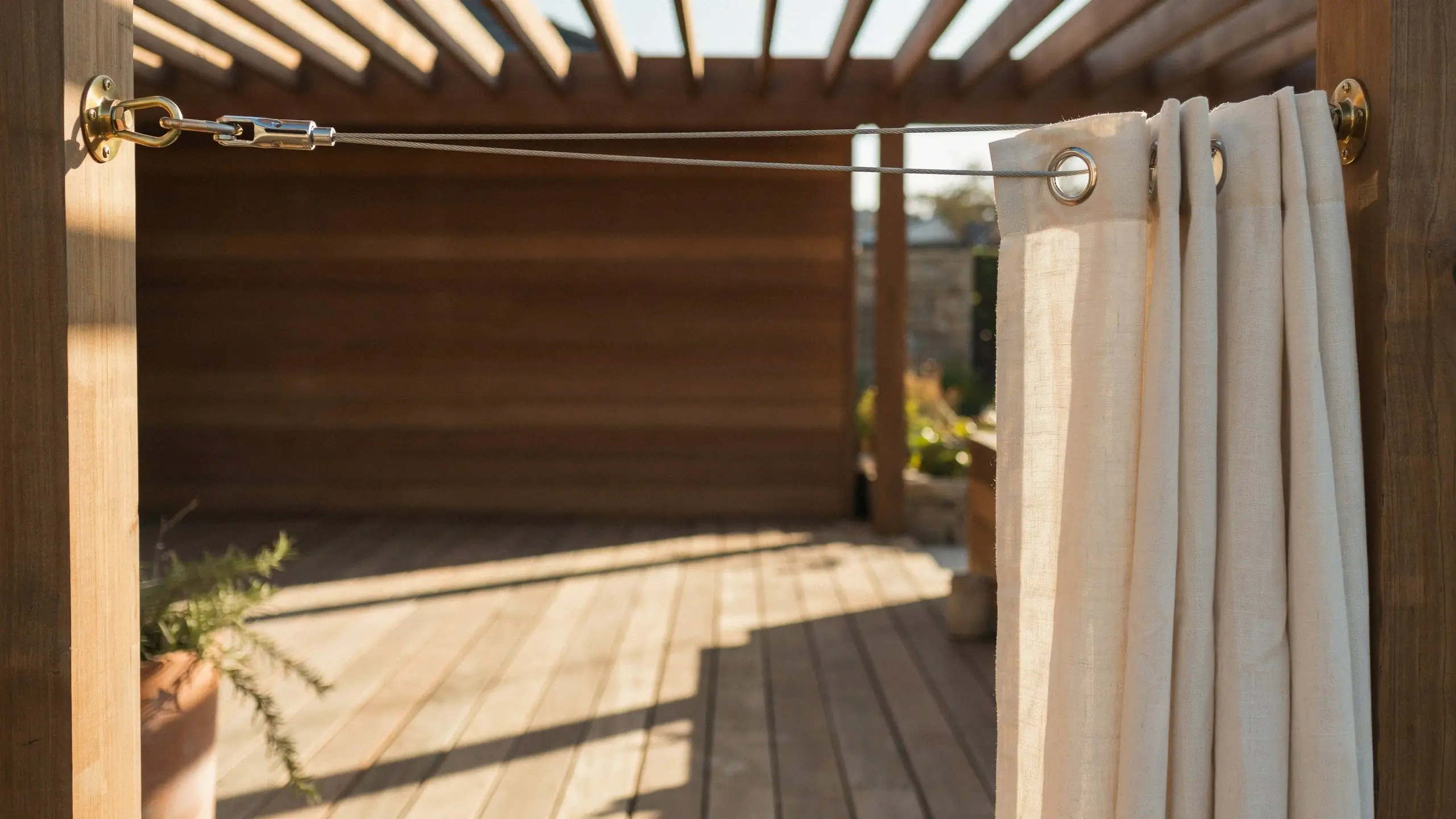 Beige grommet-style outdoor curtain suspended on a stainless steel tension wire and turnbuckle system, mounted across a wooden pergola frame for shading and privacy