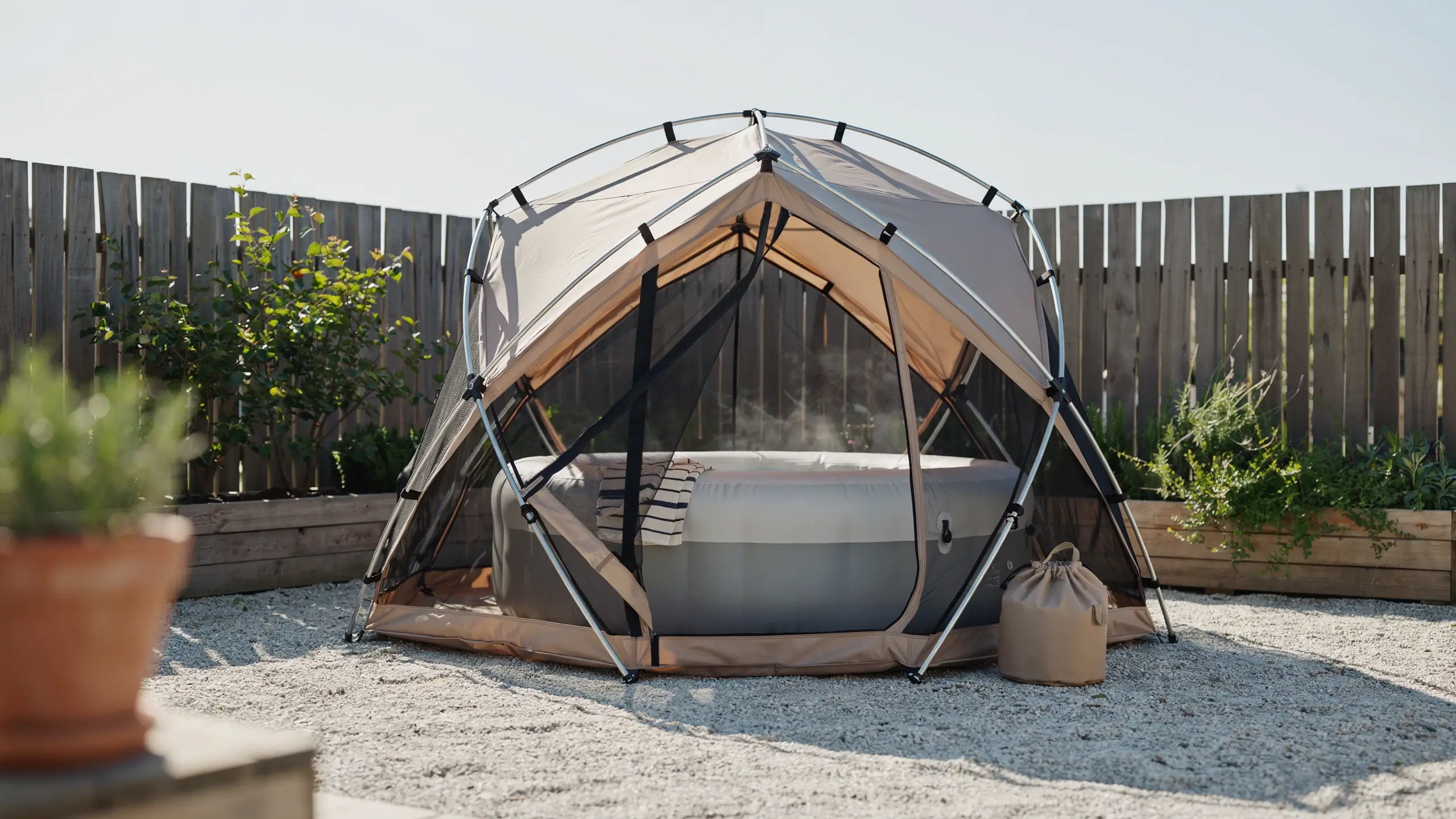 Portable pop-up privacy shelter with mesh sides enclosing a steaming inflatable hot tub on a gravel backyard patio