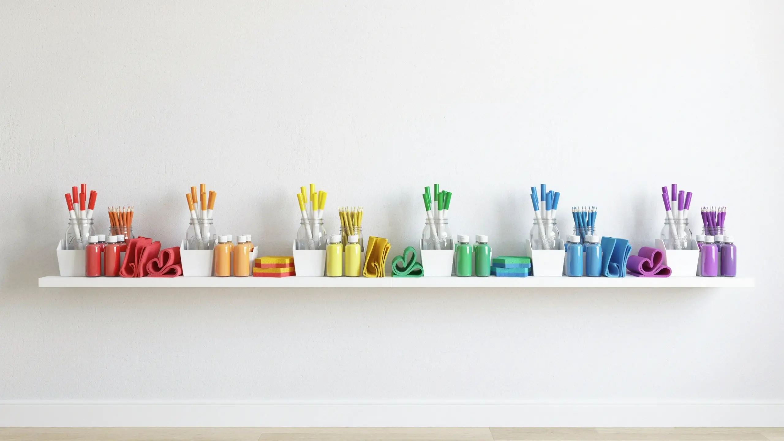 Rainbow color-coded craft supplies with paint bottles, brushes, and folded fabrics neatly organized on a white floating shelf for an aesthetic art studio. 