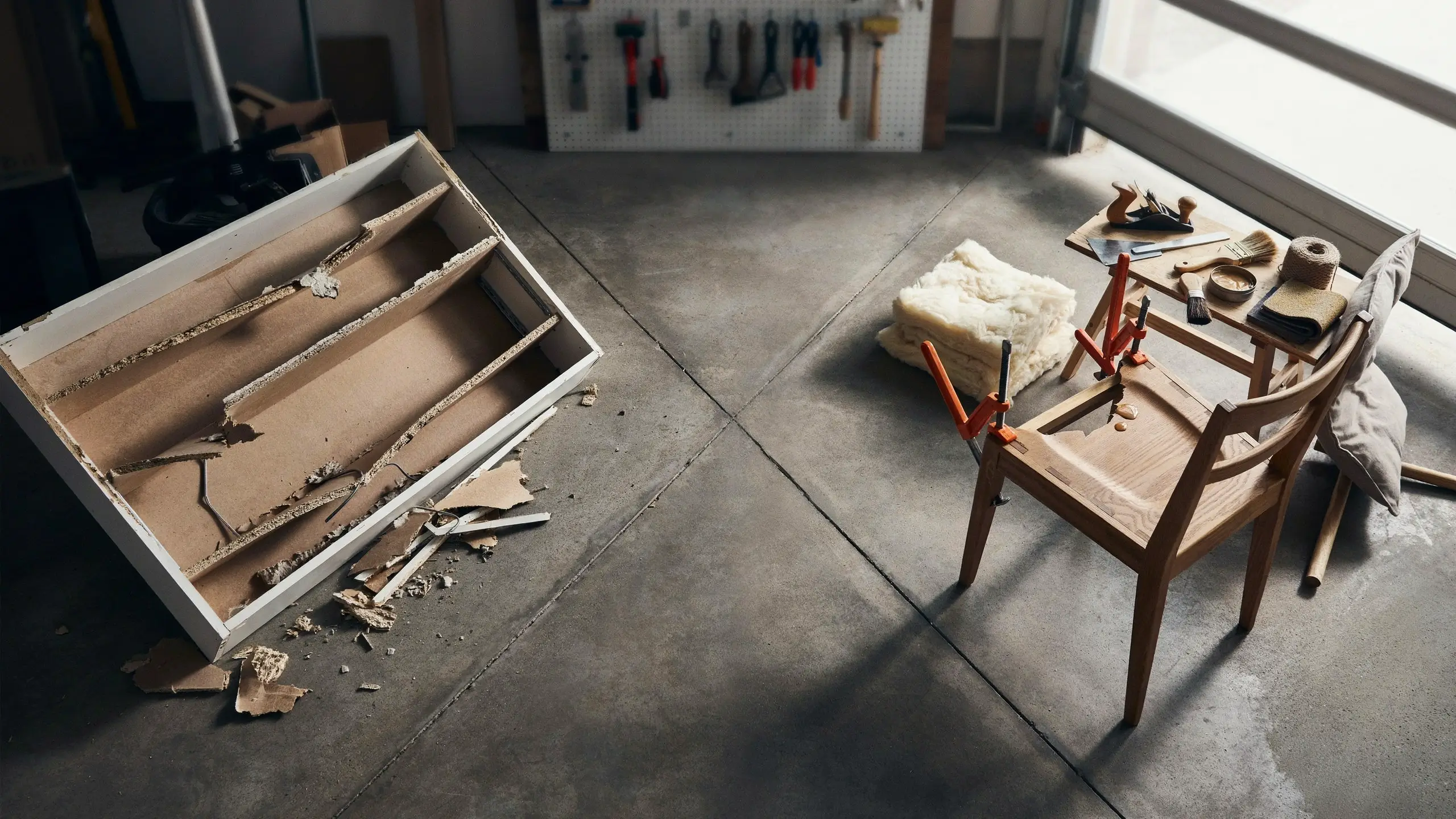 Broken particleboard furniture beside a solid wood chair being repaired in a workshop.