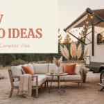 Cozy RV patio setup at a forest campsite featuring a white L-shaped outdoor sofa with rust-colored throw pillows, a small side table with coffee mugs and books, and warm bistro string lights hanging under the RV awning, next to a stone campfire ring surrounded by pine trees at sunset.