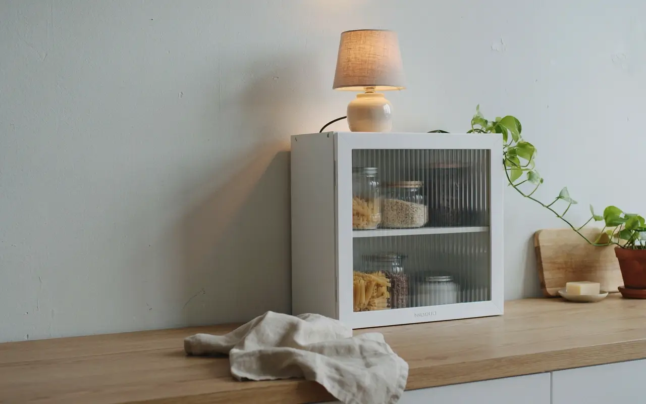 Slim IKEA KNOXHULT cabinet on a kitchen counter used as a vertical pantry with ribbed glass doors.